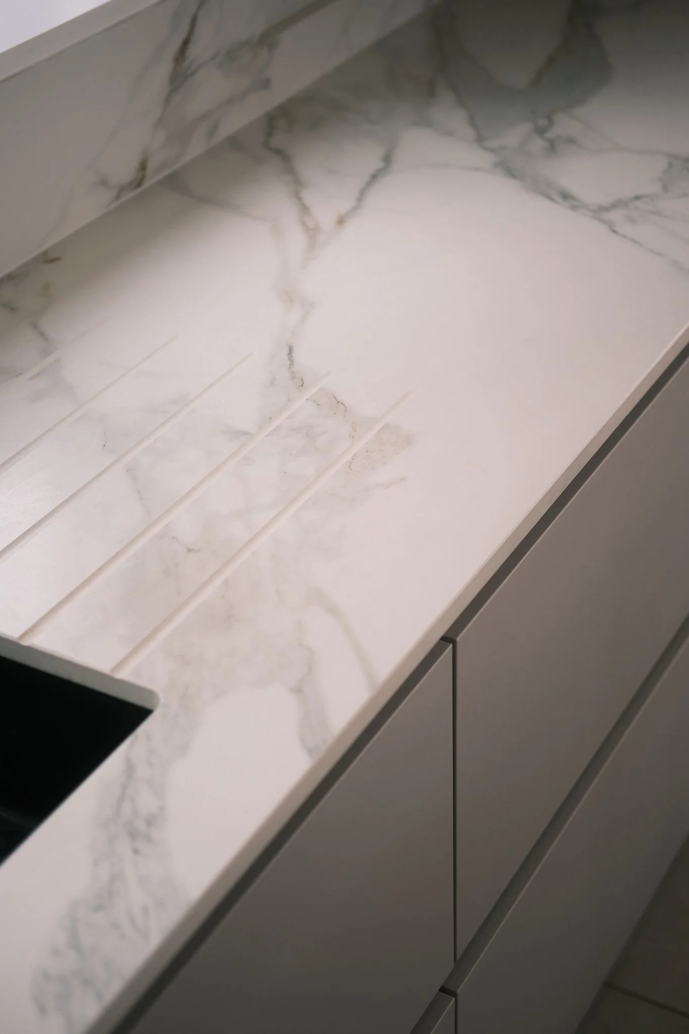 Close-up of a white marble countertop with gray veining in a modern kitchen with gray cabinets.