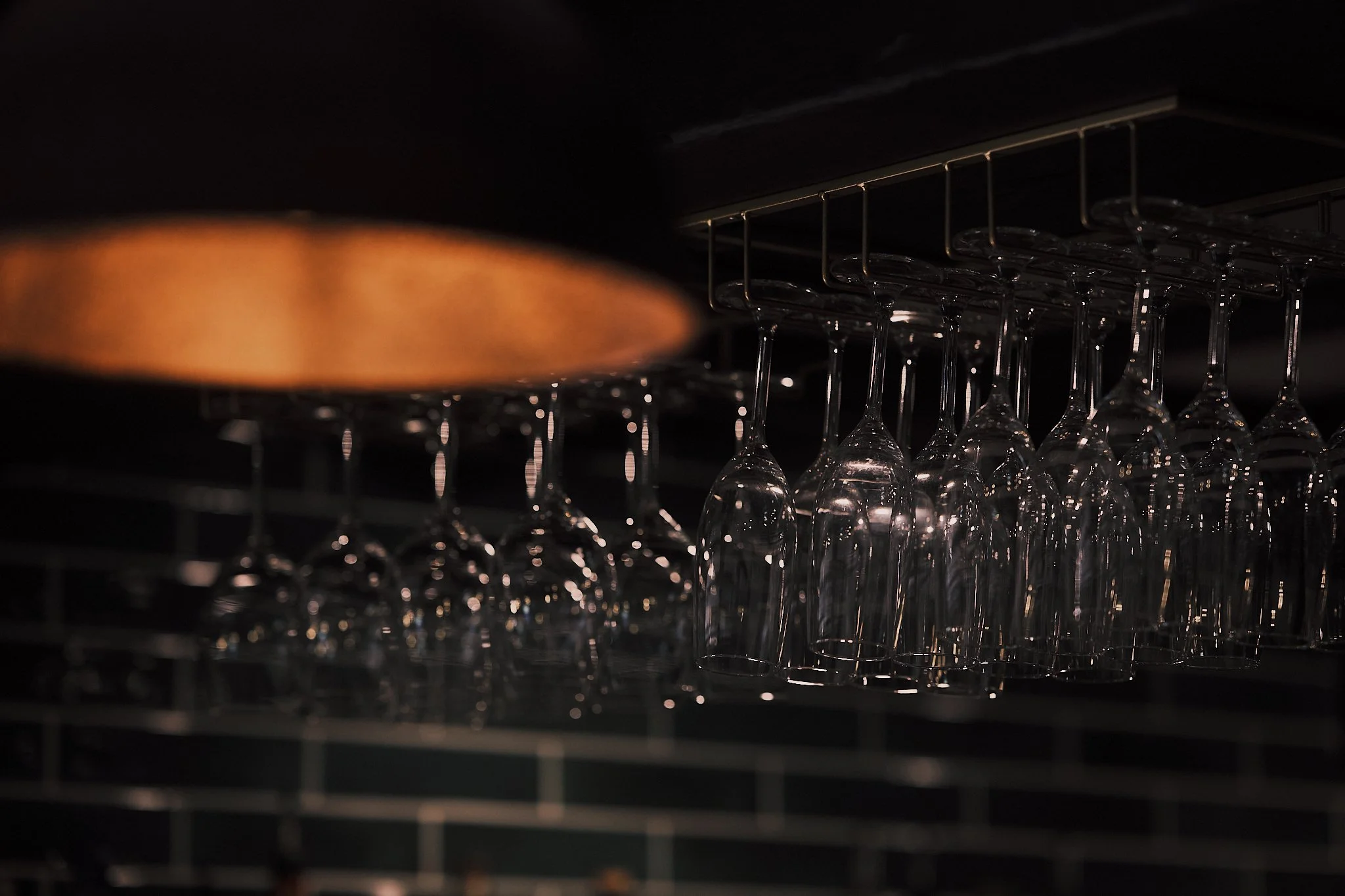A dimly lit wine glass rack with upside-down wine glasses hanging from metal hooks in a bar or restaurant.