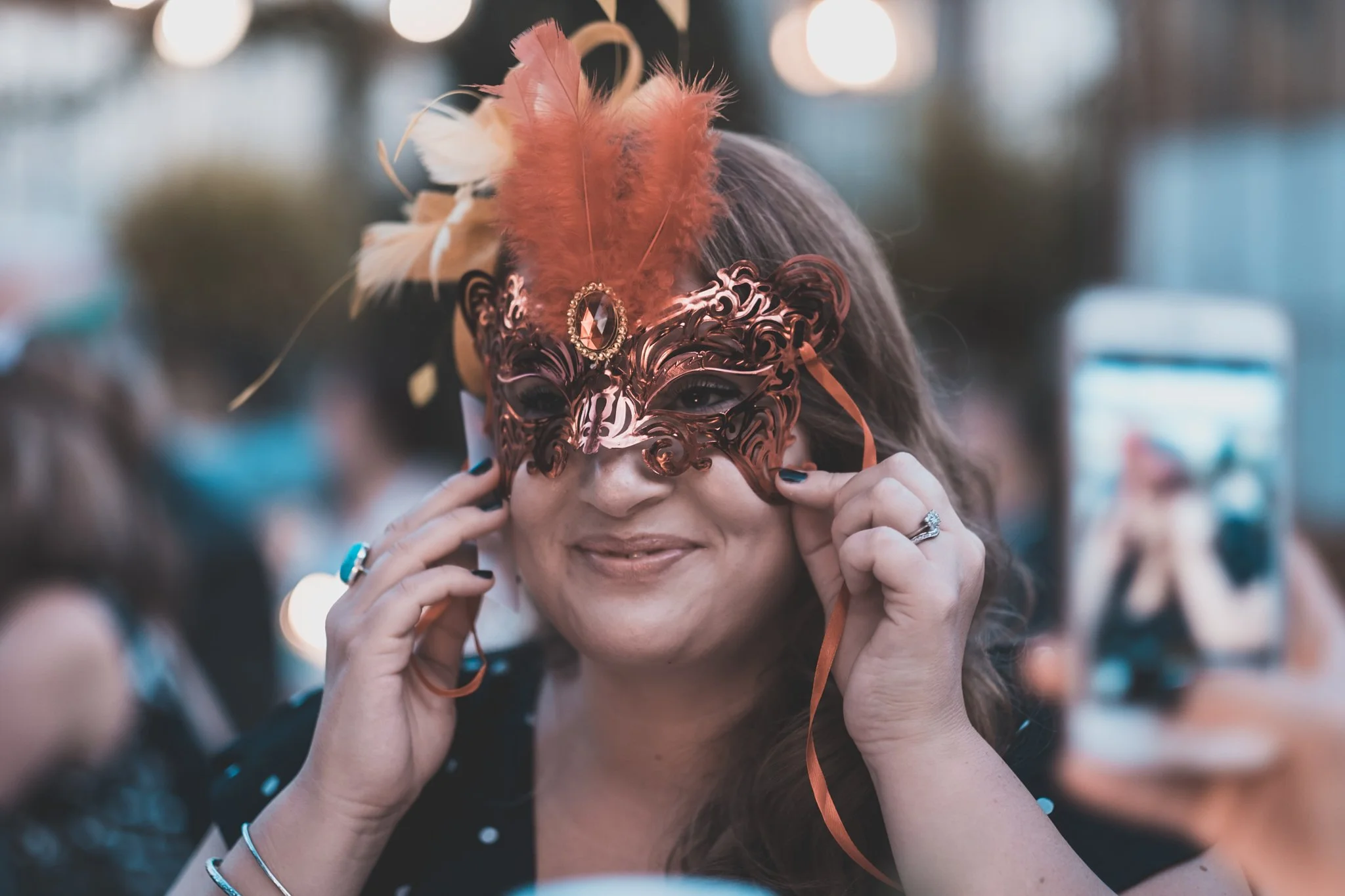 Woman wearing a decorative, metallic mask with an orange feather, at a festive event.