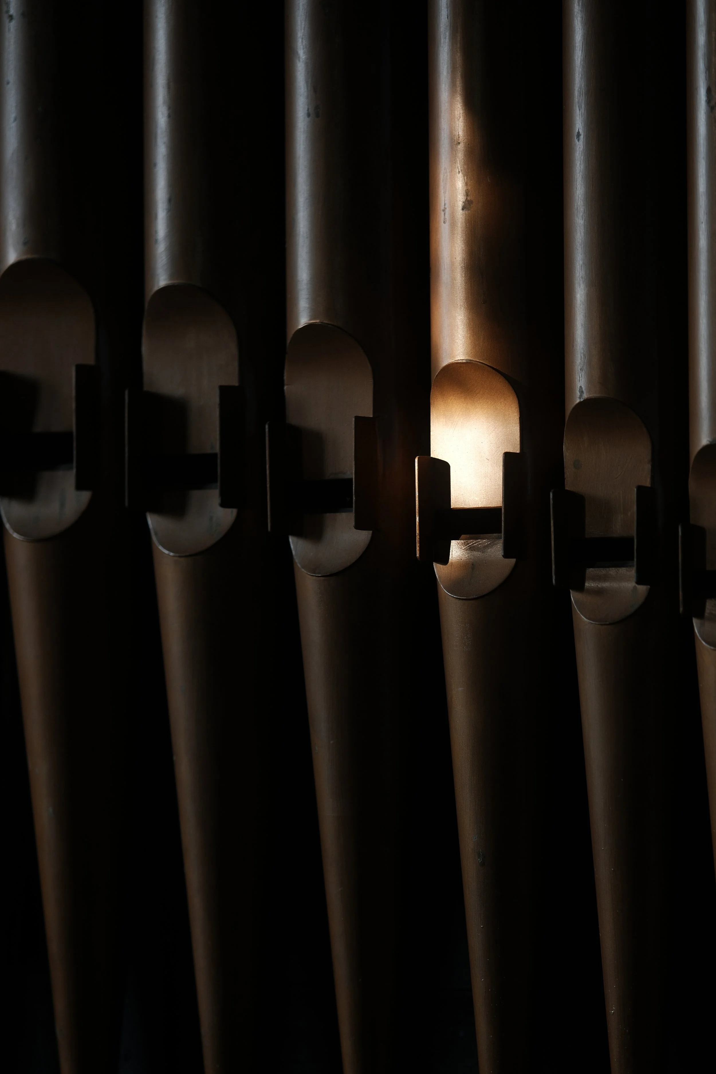Close-up of a pipe organ with sunlight shining through the pipes, creating reflections and shadows.