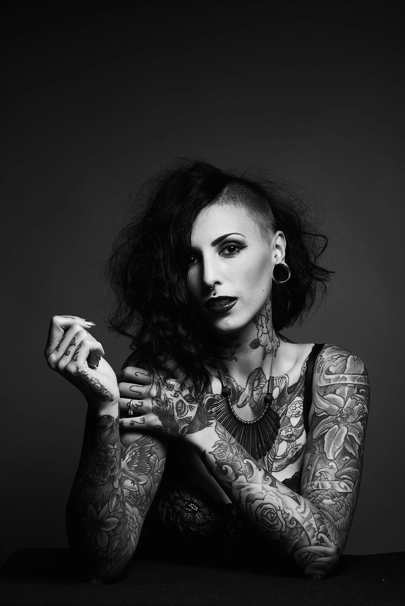 Black and white portrait of a tattooed woman with dark lipstick and edgy hairstyle, looking at the camera.
