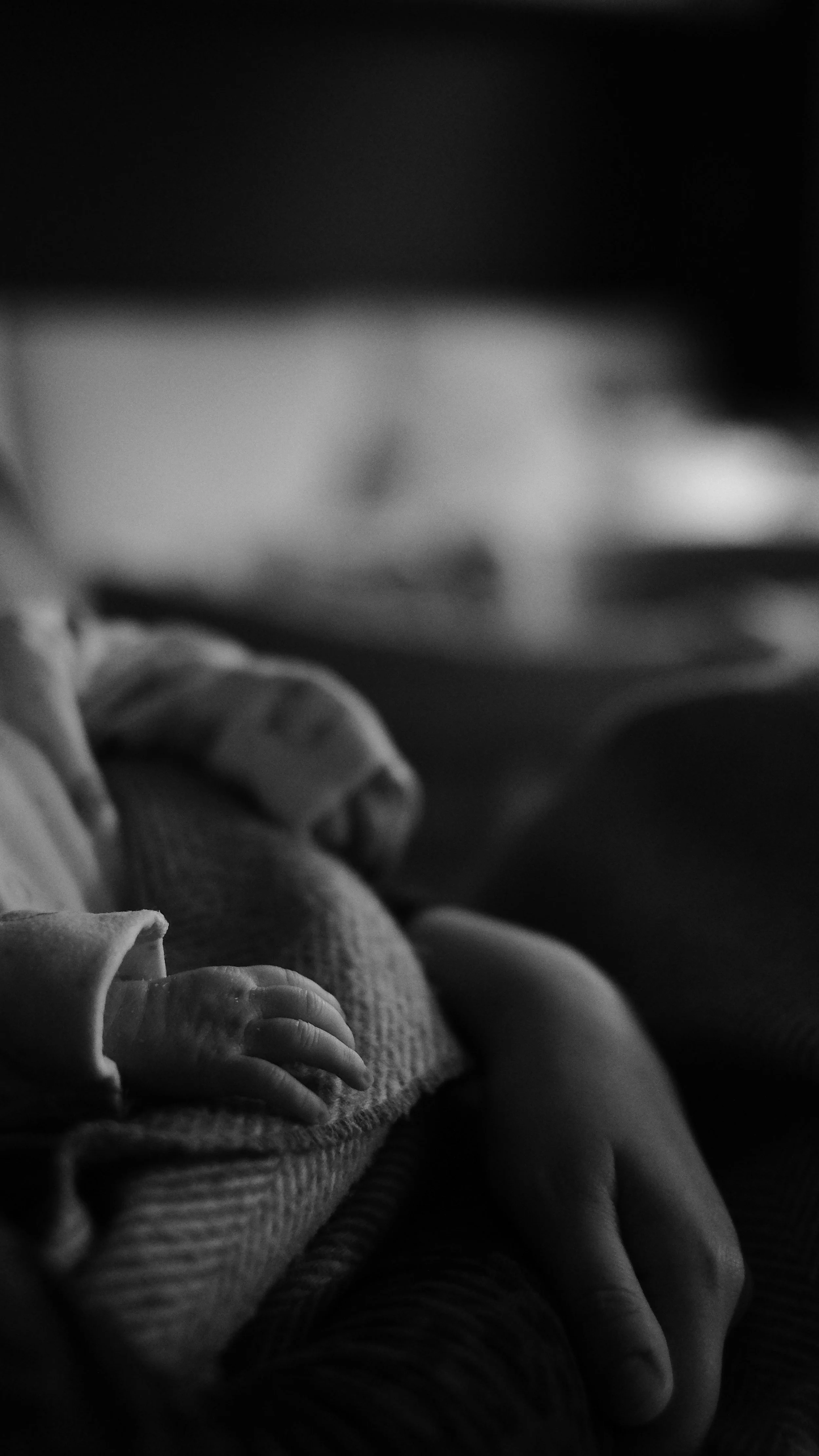 Close-up of a sleeping infant's hand resting on the adult's arm in black and white.