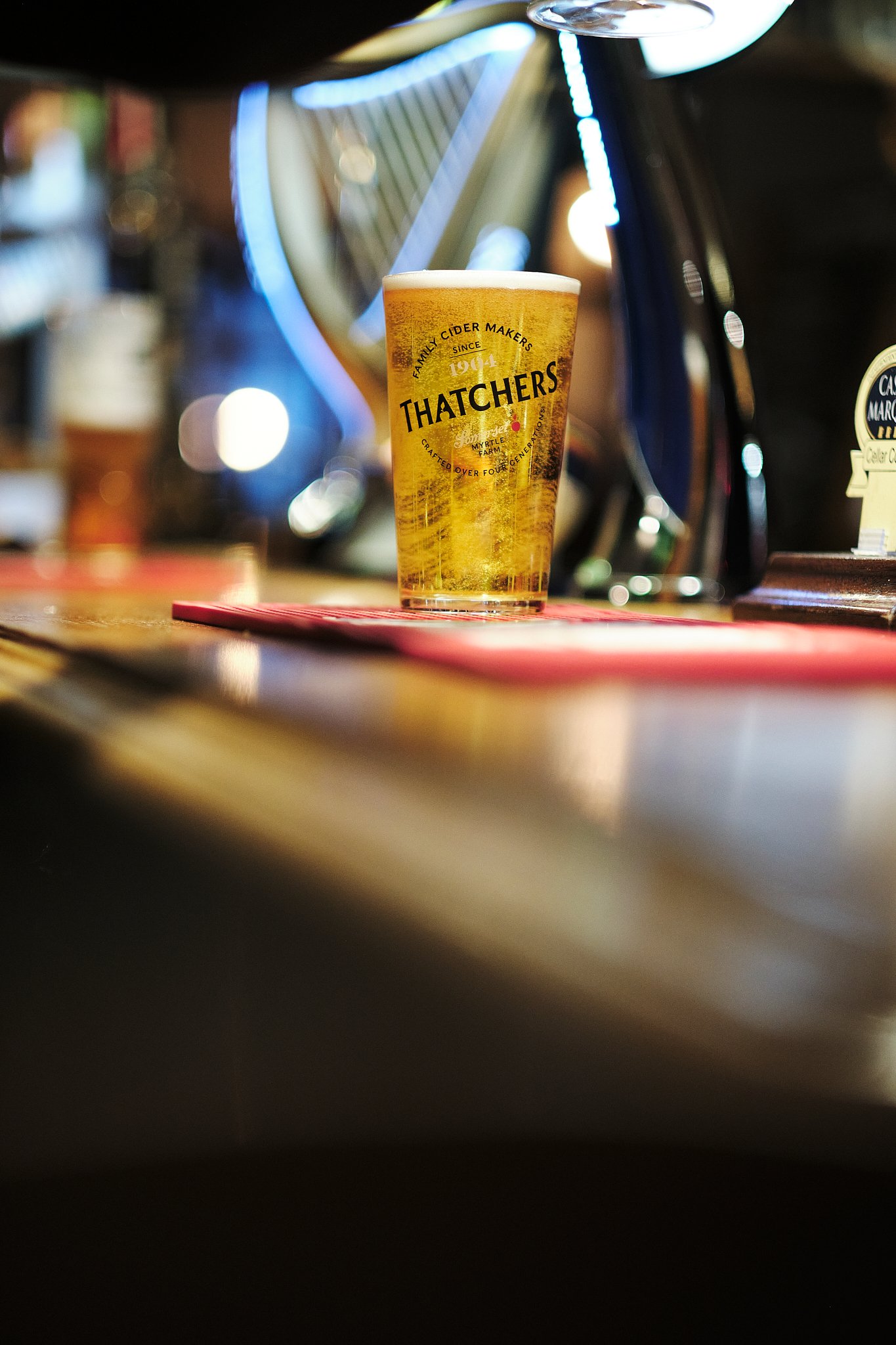 A glass of beer on a bar counter with a blurred background, featuring a harp and round lights.