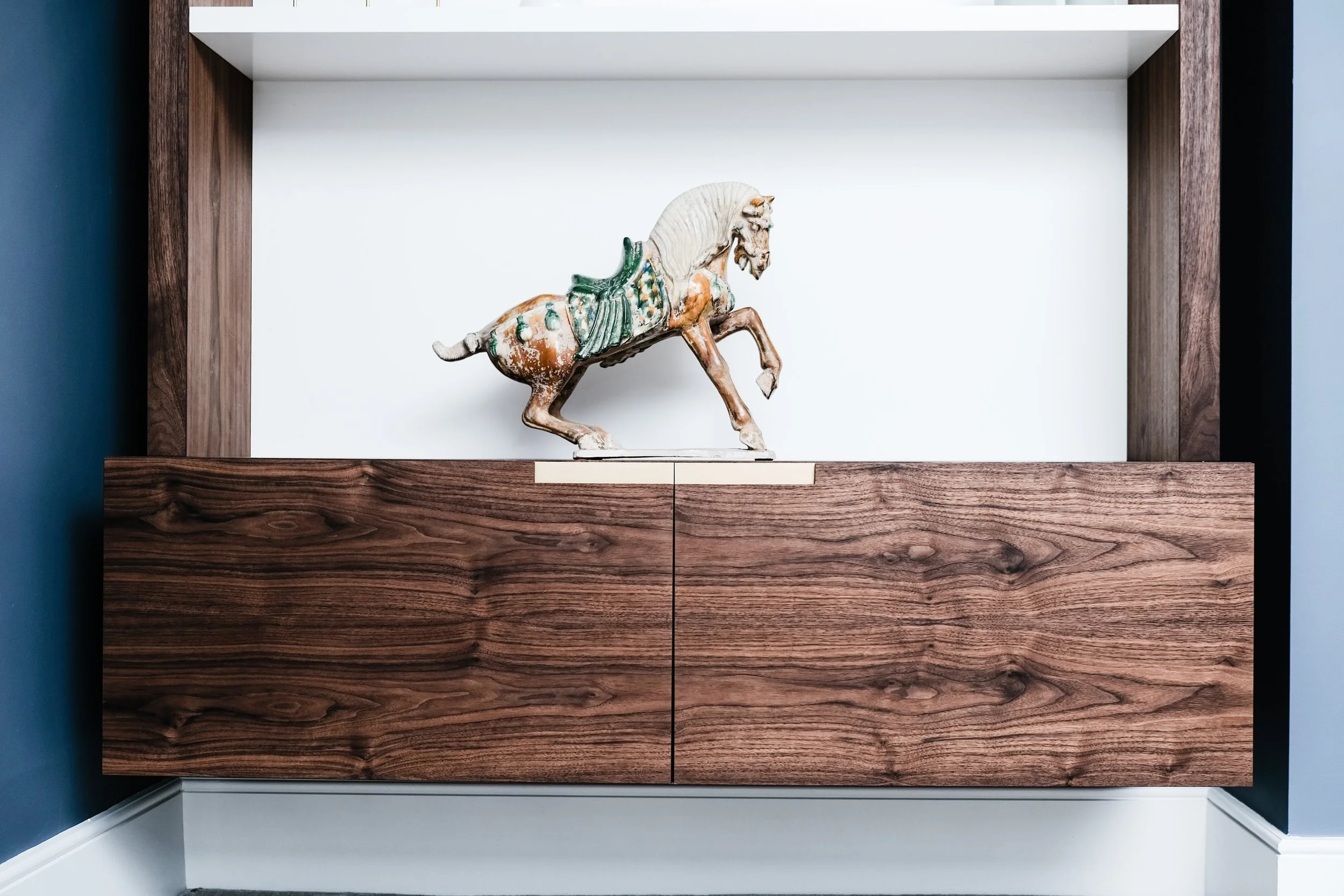Decorative ceramic horse sculpture on a wooden cabinet against a white wall in a modern interior.