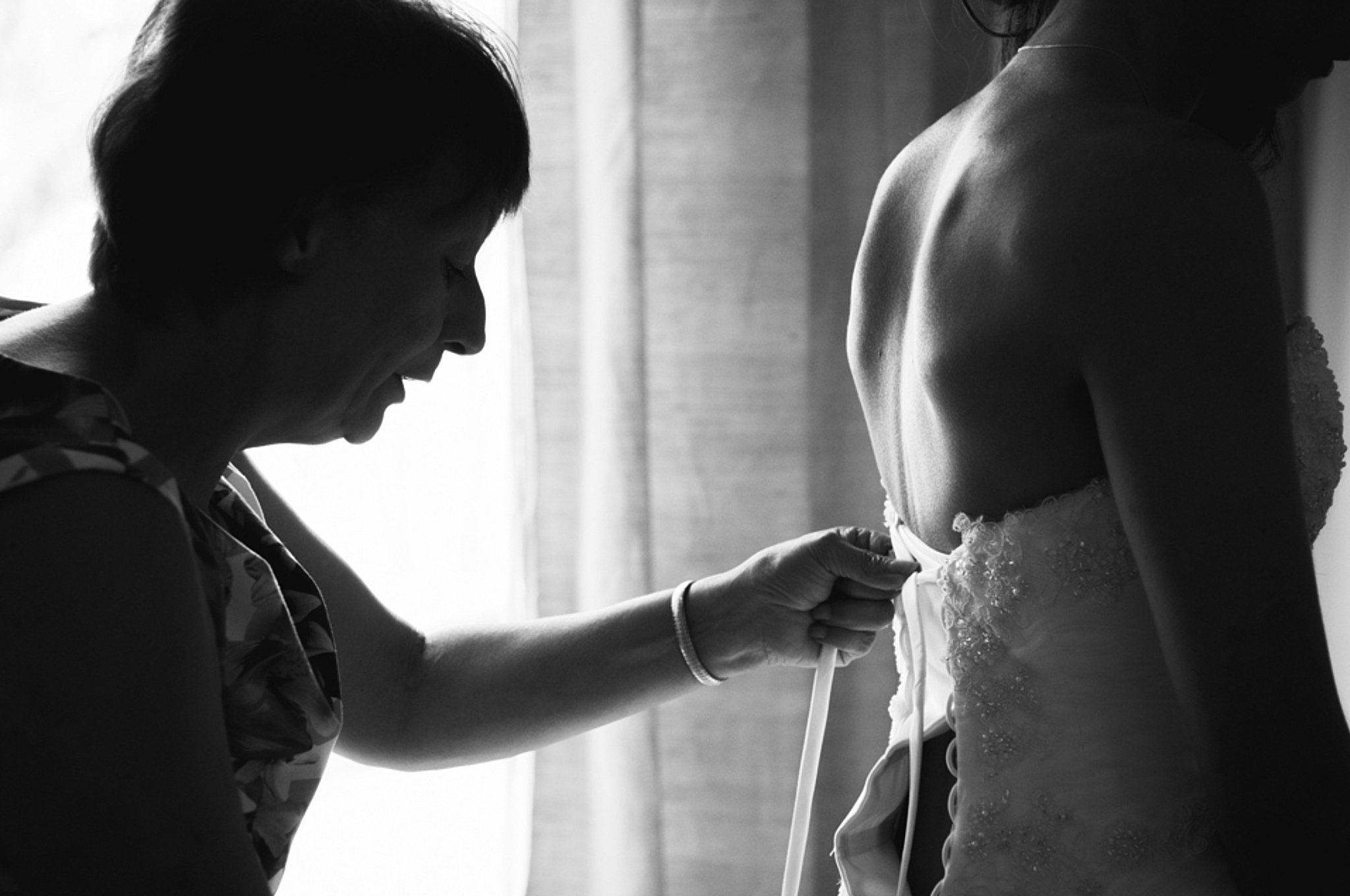 A woman helping a girl close the back of her wedding dress.