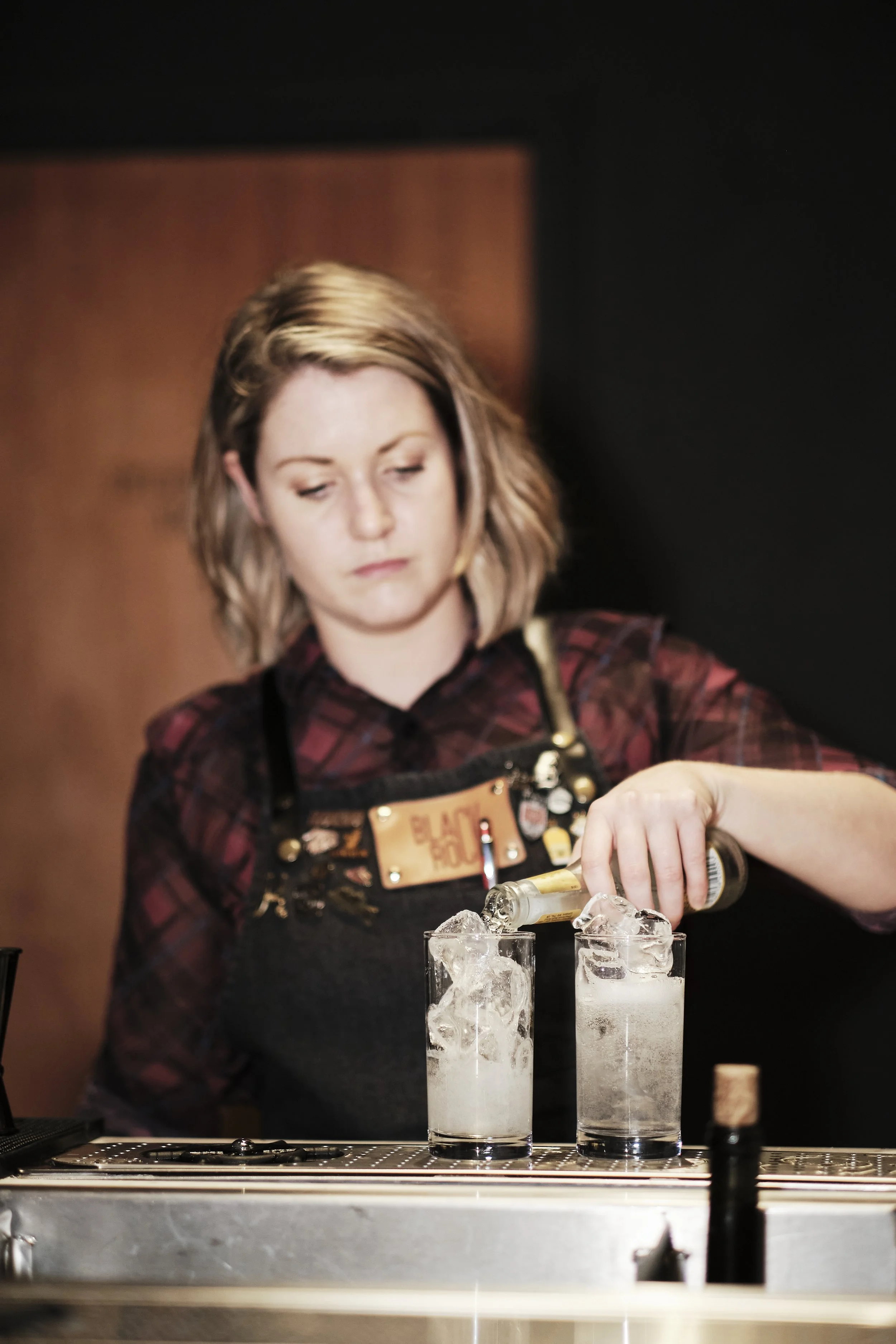Bartender pouring alcohol into two glasses filled with ice.
