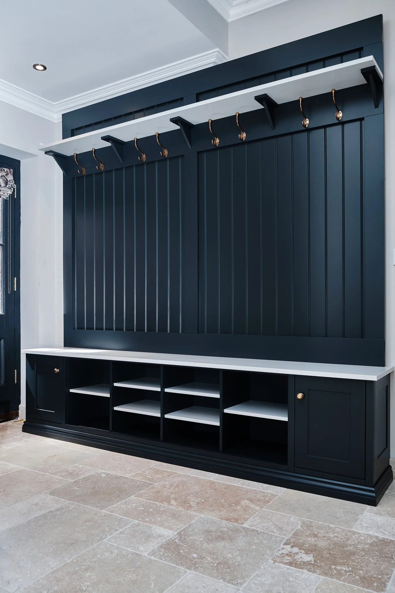 A stylish navy blue and white mudroom or entryway storage unit with hooks, cubbies, and cabinets, set against a beige tiled floor and white walls.