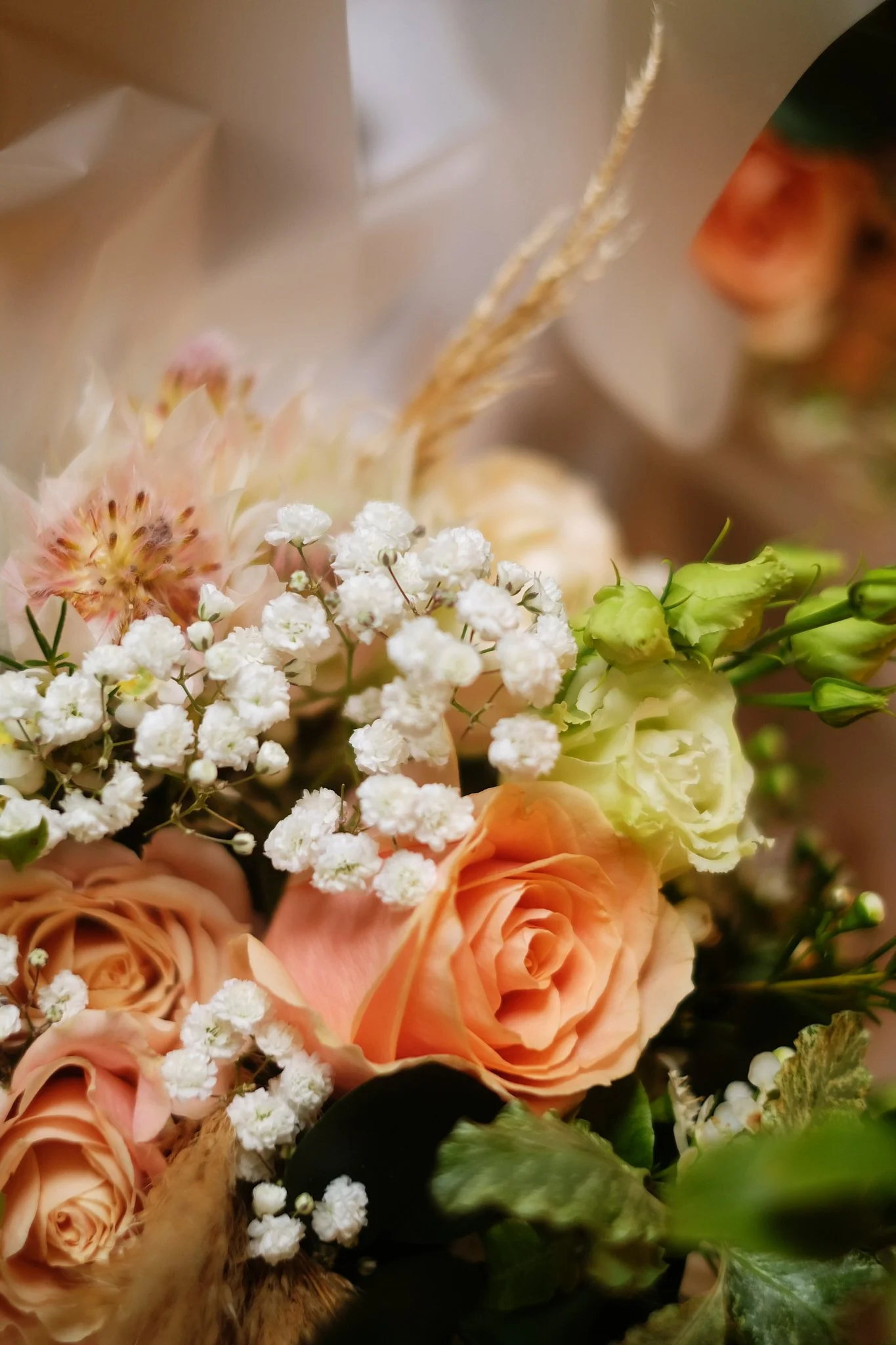Close-up of a floral arrangement with peach roses, white baby's breath, and greenery.