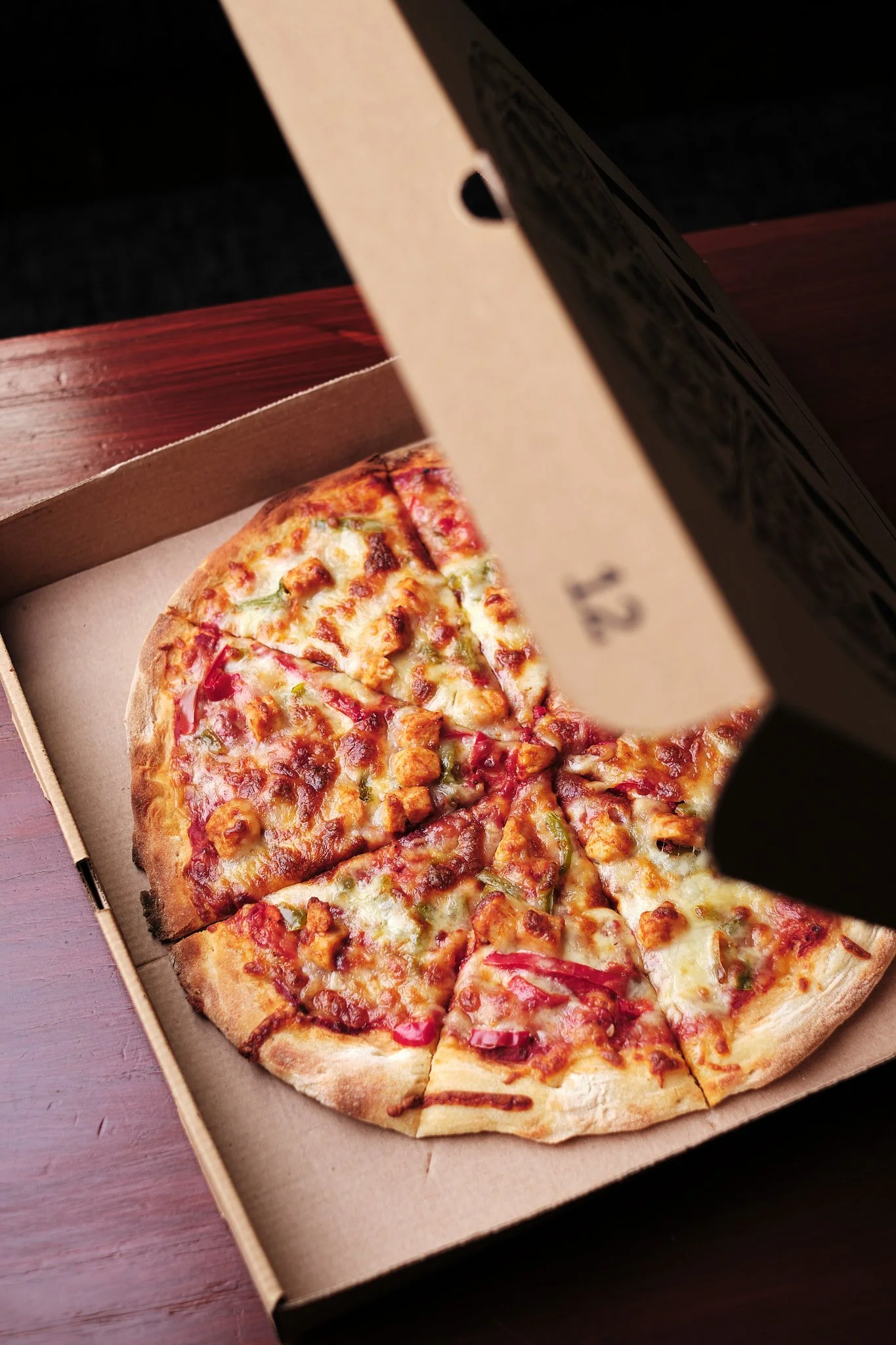 Half-eaten pizza in a cardboard box on a wooden surface.