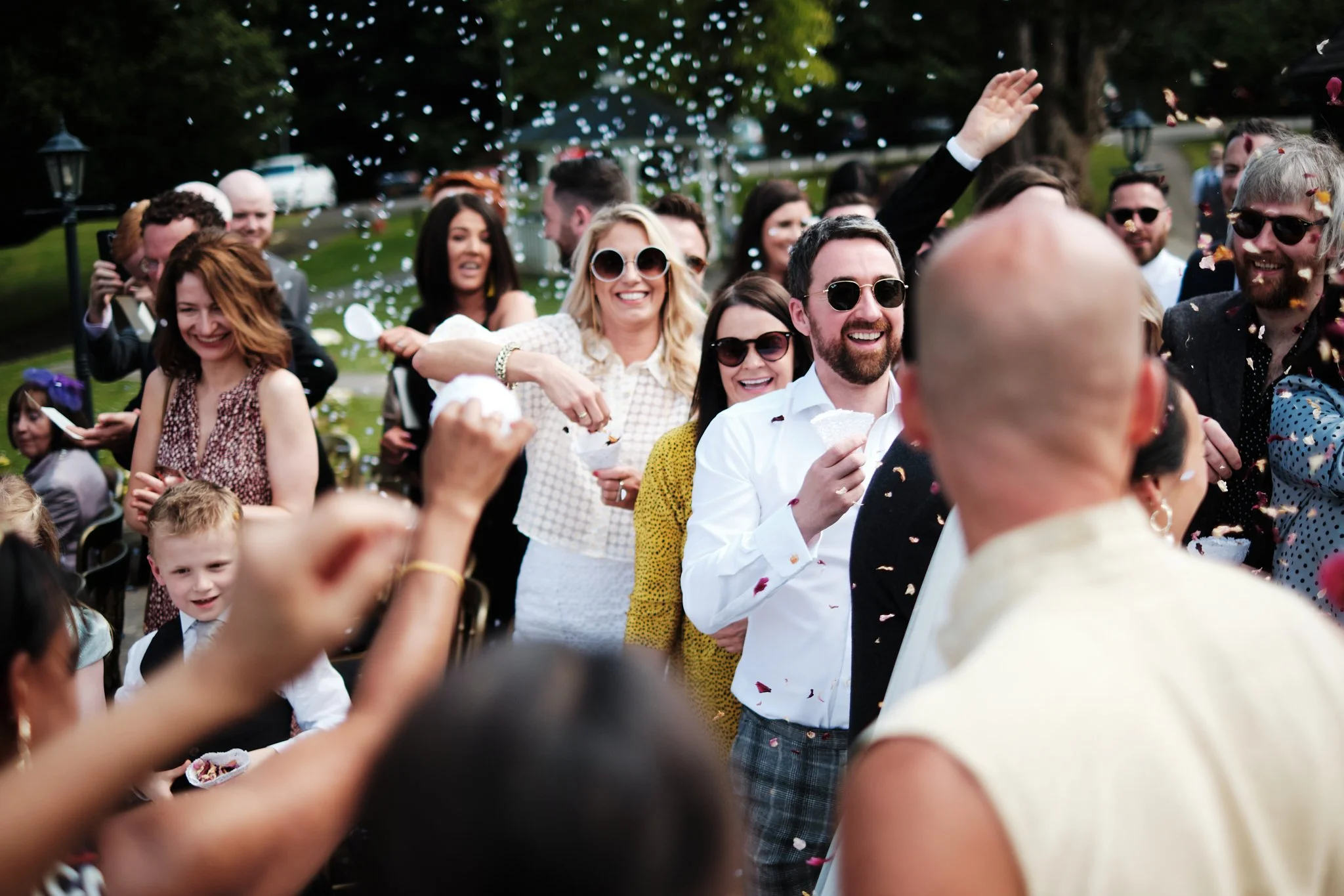 Group of people celebrating outdoors, smiling, with confetti falling around them.