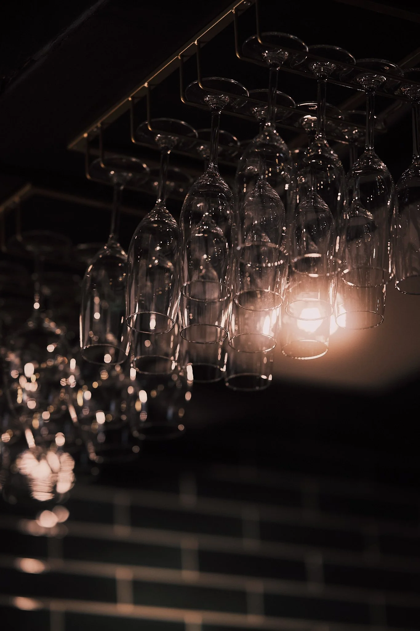 Hanging glassware under a dim light in a bar or restaurant setting.
