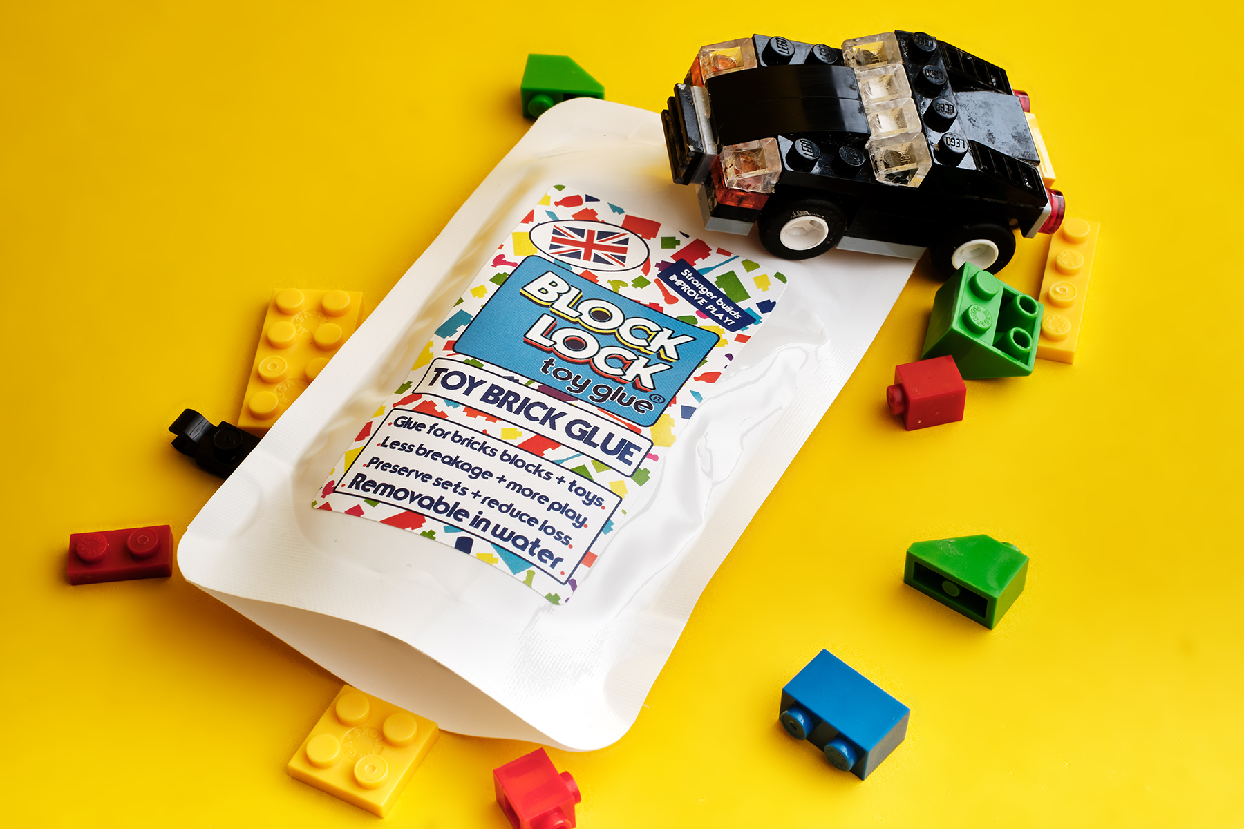 Toy brick glue package with scattered LEGO-style building blocks on a yellow background.