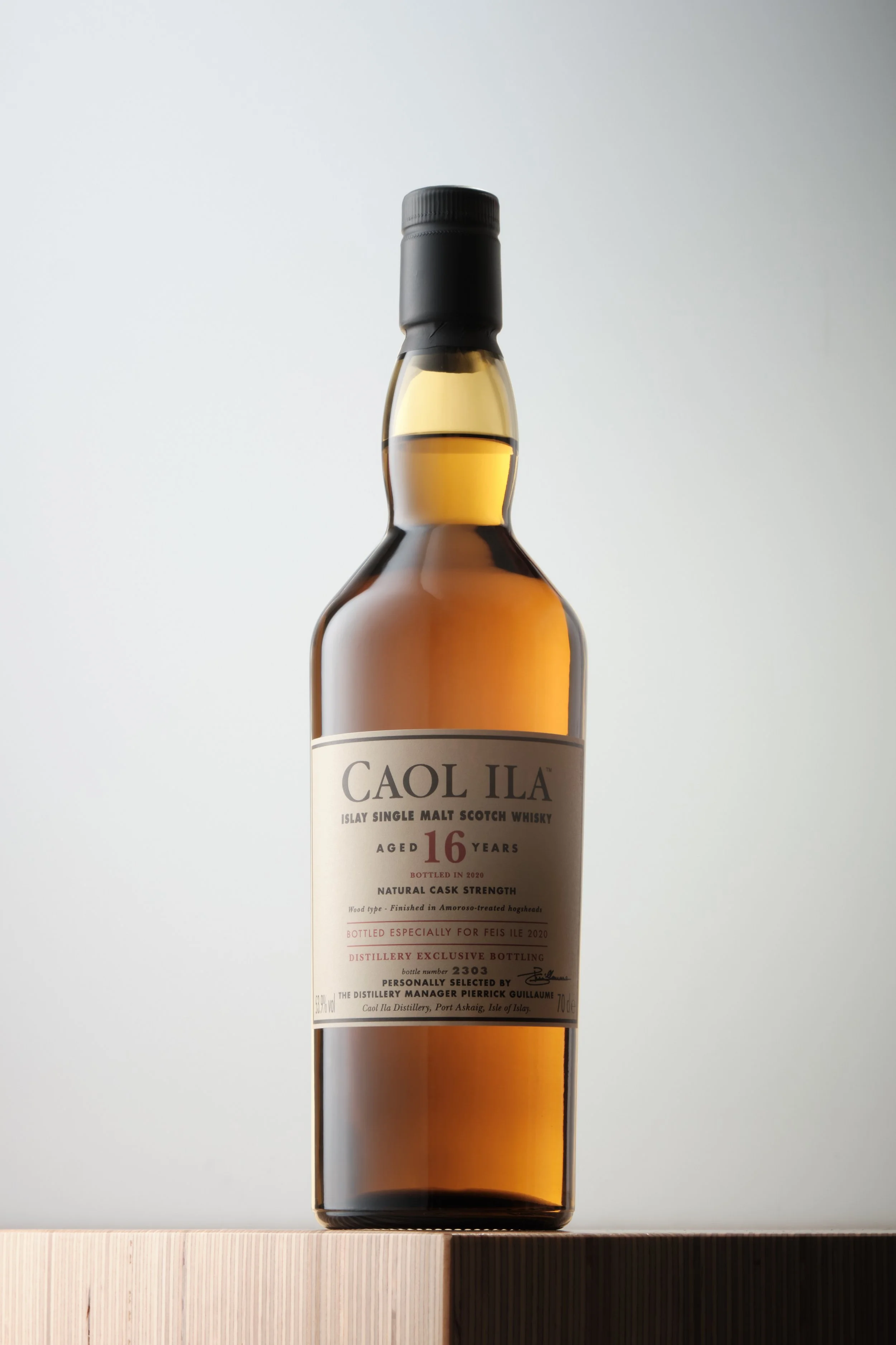 A bottle of Caol Ila single malt Scotch whisky with a white label, placed on a wooden surface against a plain background.