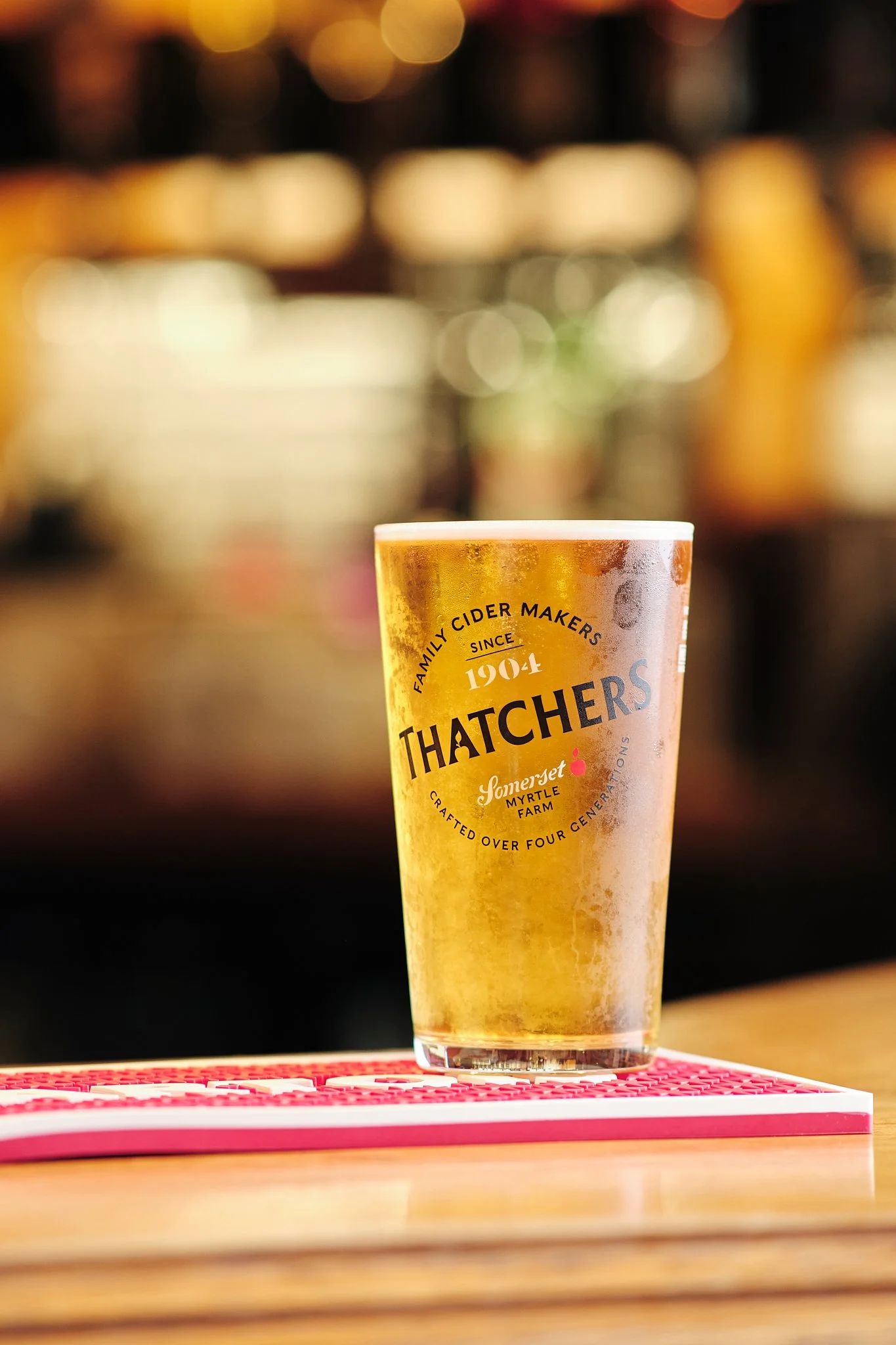 A glass of cider on a bar with a blurred background of bottles, with condensation on the glass.