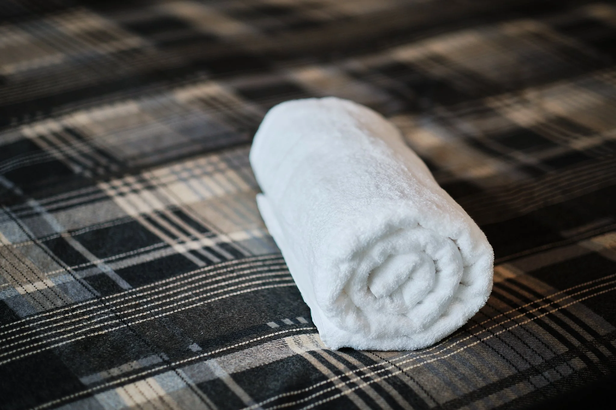 A white towel rolled up on a checkered fabric surface.