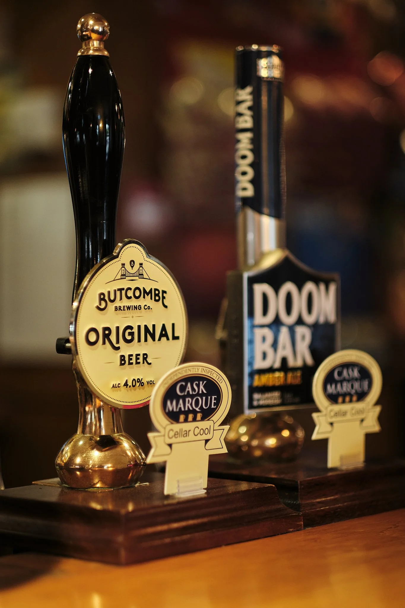 Beer tap with Butcombe Brewing Co. Original Beer label and Doom Bar tap handle on a wooden bar counter.