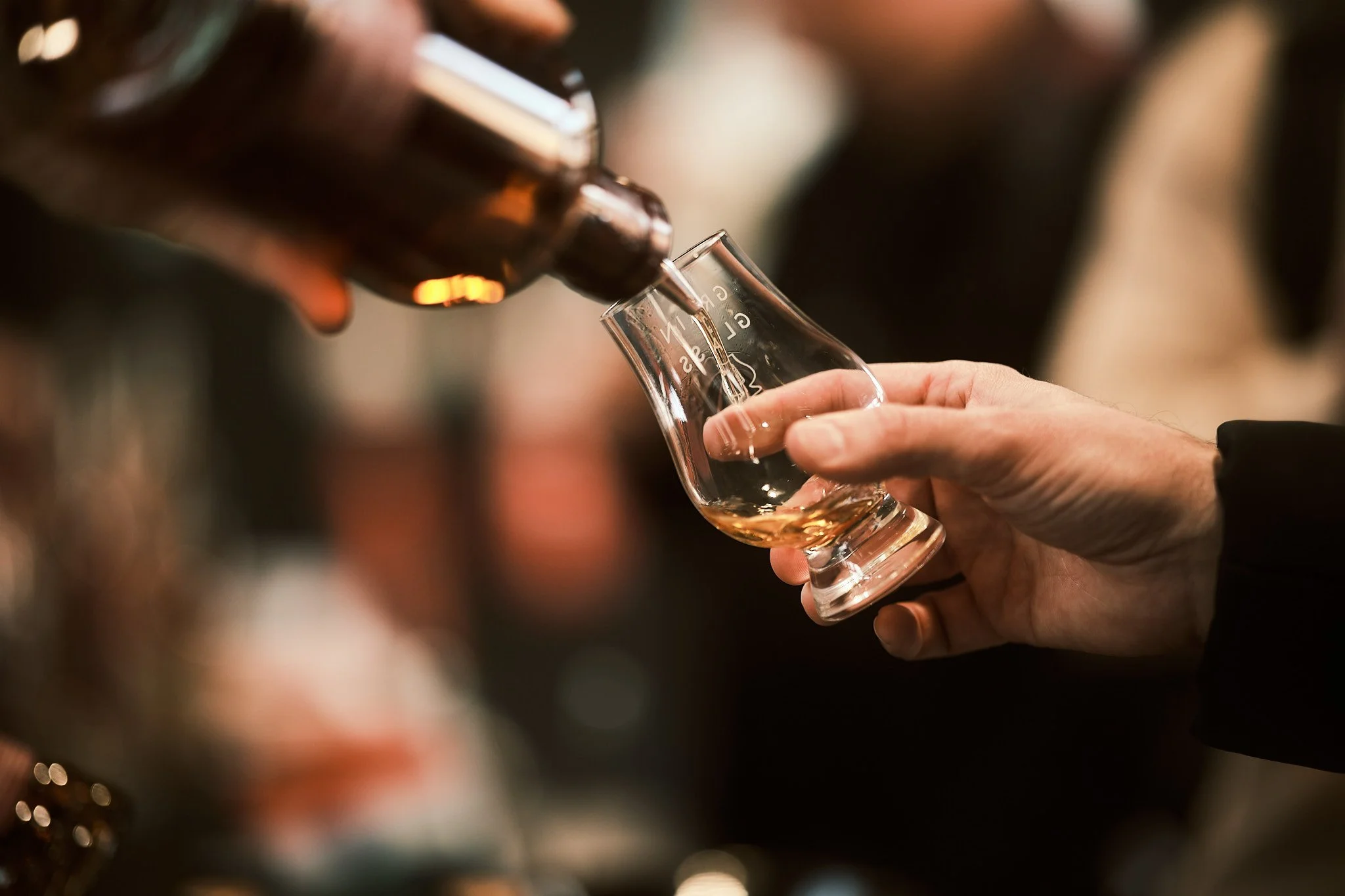 Person pouring whiskey into a glass from a bottle at a bar.