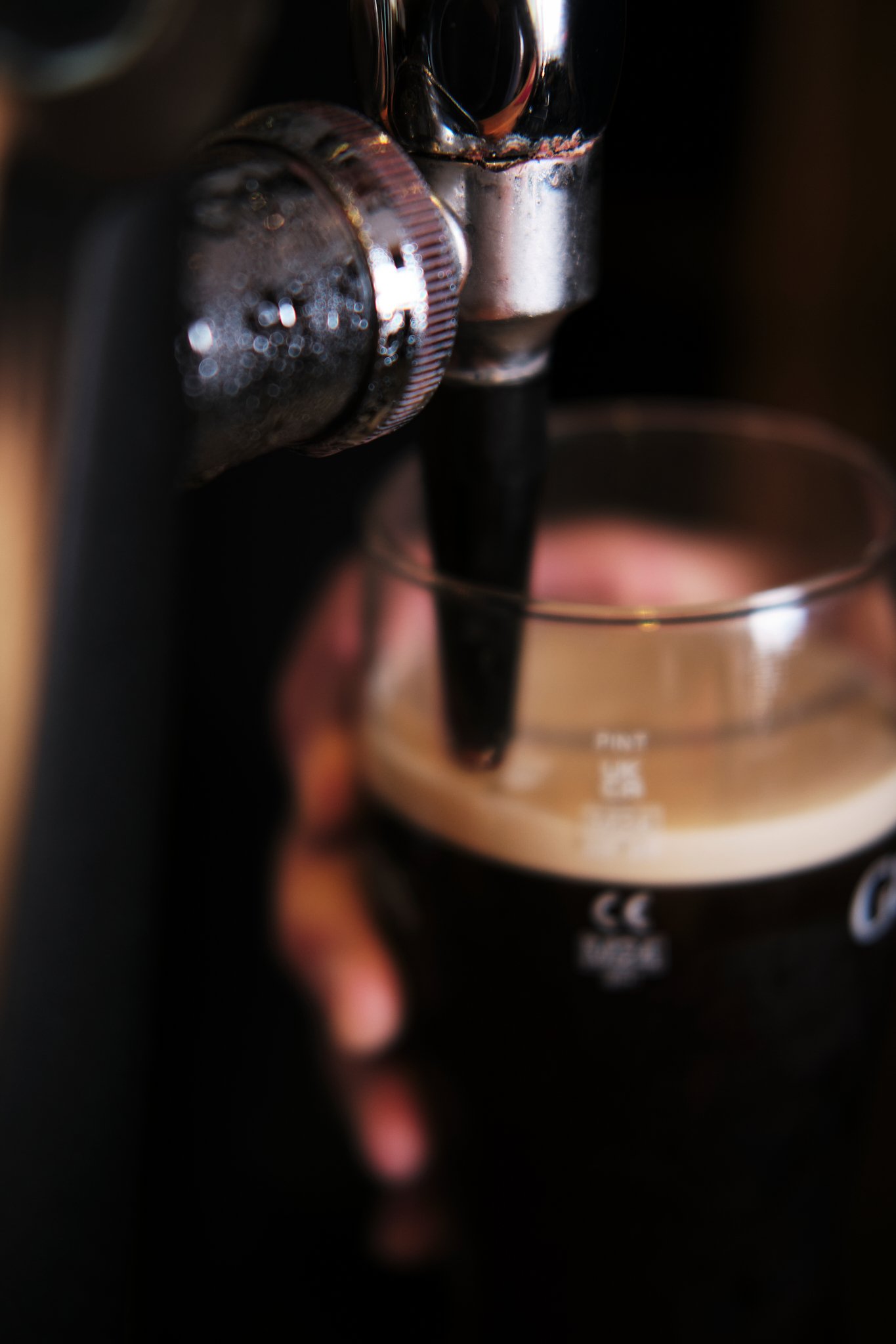 Close-up of a coffee espresso machine pouring dark coffee into a clear cup with some foam on top.