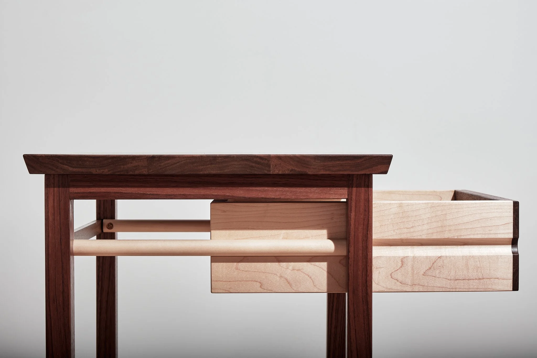 Part of a wooden table with a two-tone design, featuring dark and light wood, against a plain white background.