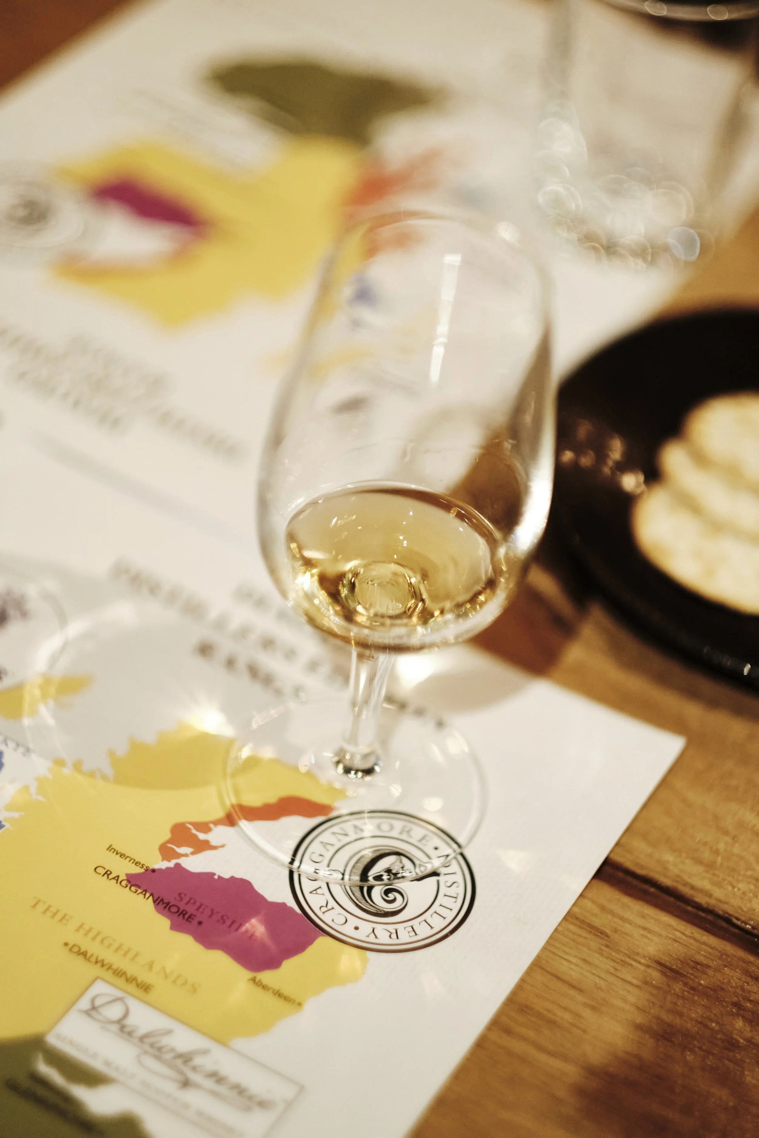 Glass of white wine on a table with a partial map of Ireland underneath, and a dish with food in the background.