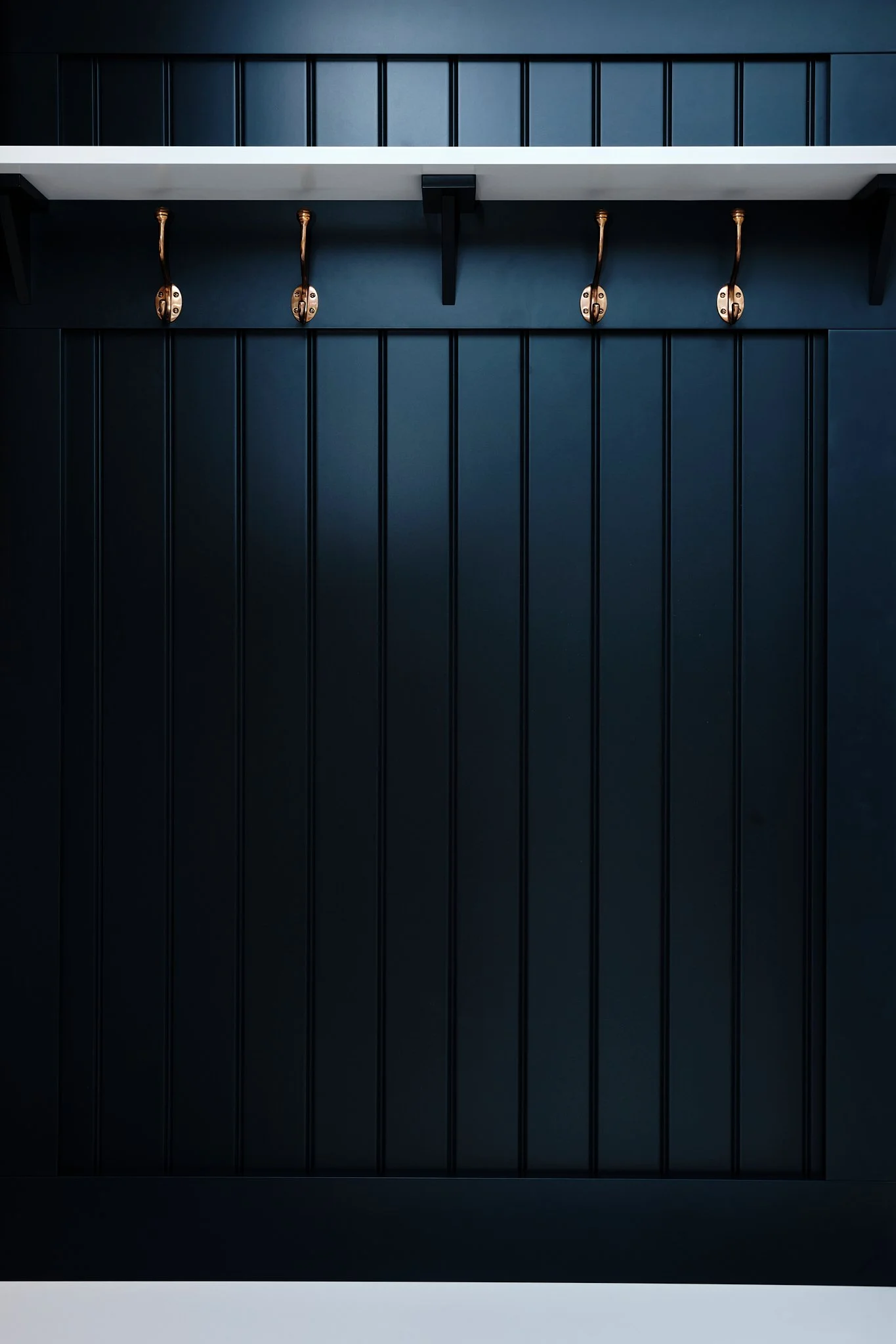 Black wooden cabinet with vertical panels, gold hooks, and a white shelf above.