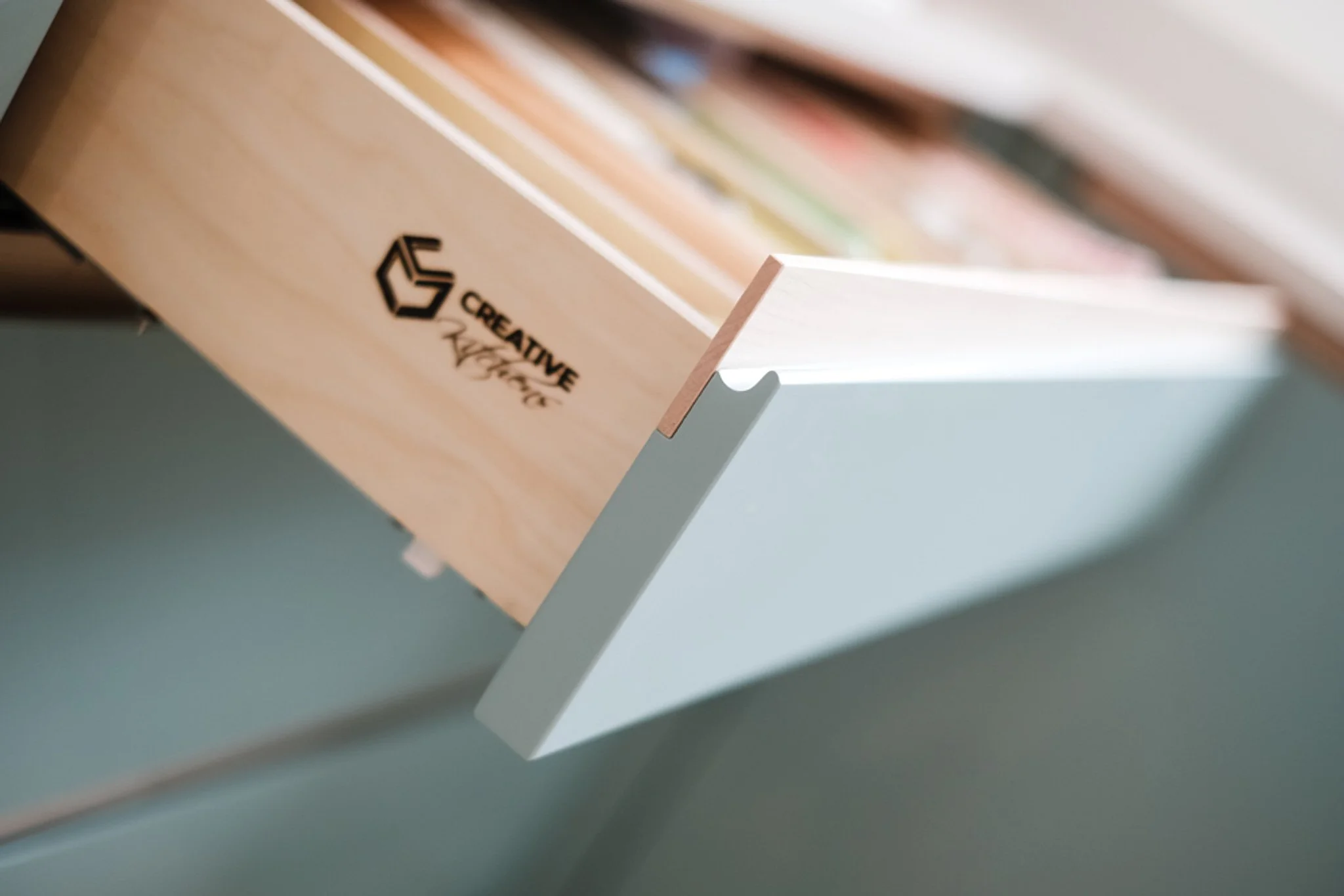 A light wood bookshelf with a black logo that says 'Creative' on the side, holding books, with part of a pale green wall visible.