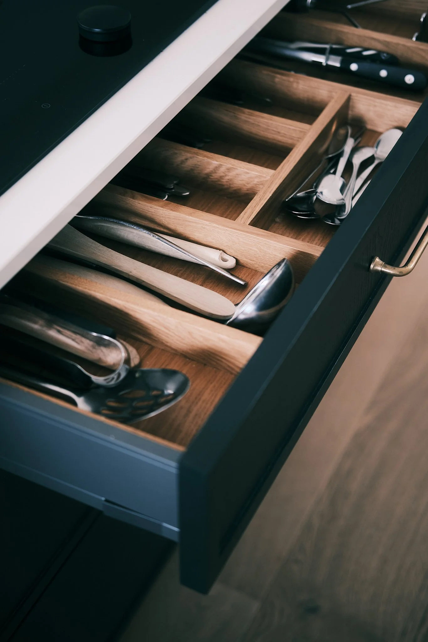 Kitchen drawer with wooden dividers containing stainless steel and wooden-handled utensils.