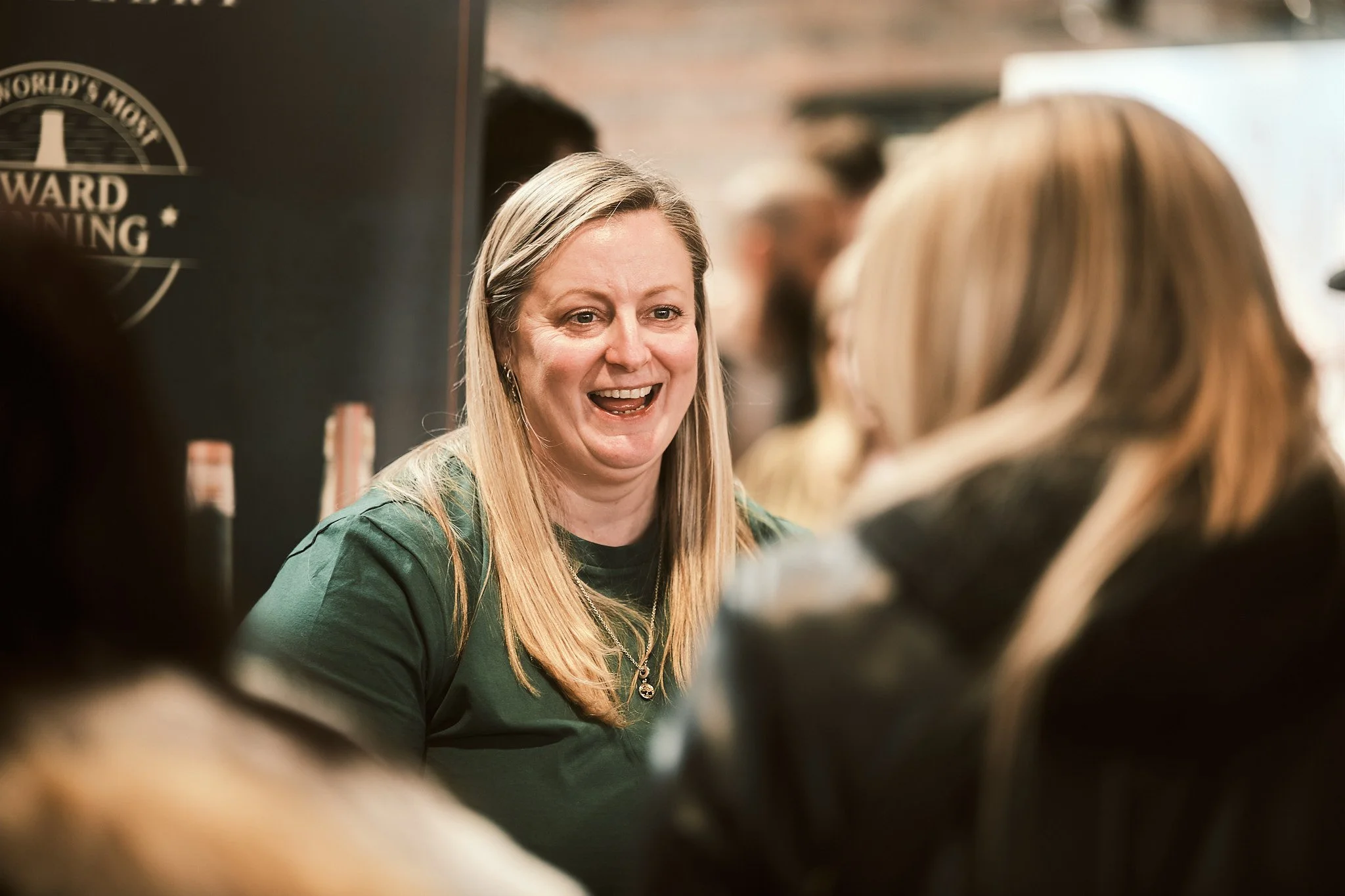 A woman with blonde hair smiling and talking to another woman with blonde hair at a social gathering or event.