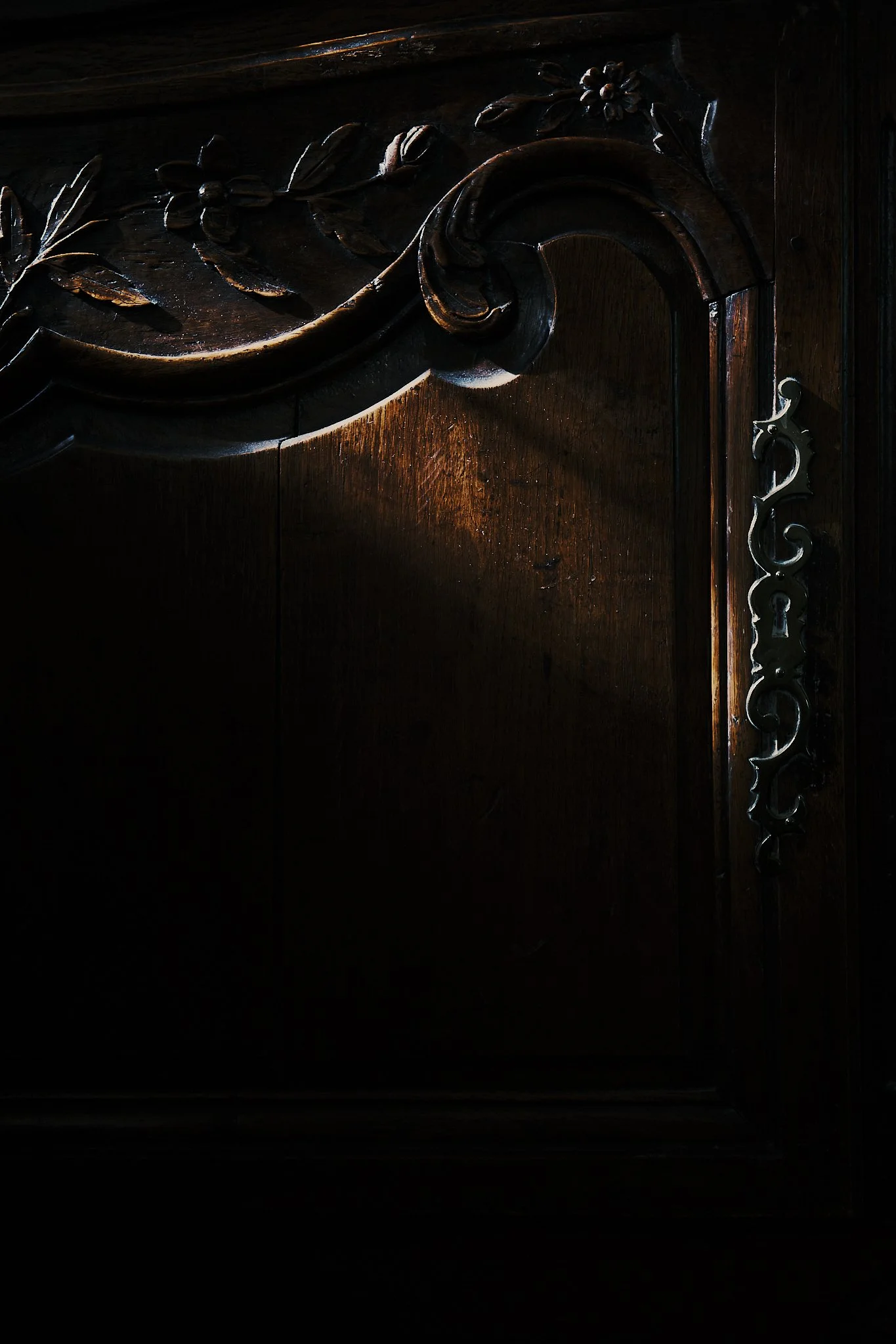 Close-up of a dark wooden furniture piece with carved floral and leaf patterns, accentuated with a subtle light glow. Hotel interior photography at THE PIG-in the Cotswolds