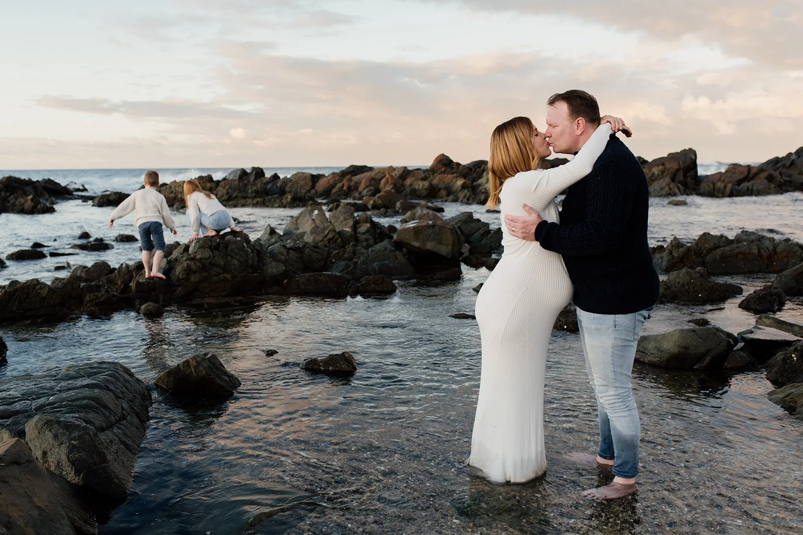 Northern Rivers family photographer captures parents kissing while children play in rock pools.