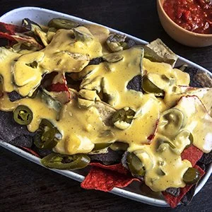 Tacos topped with melted cheese, slices of jalapeños, and diced vegetables served on a platter with a side of salsa.