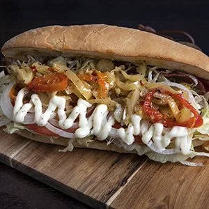 Sub sandwich with shredded lettuce, sliced tomatoes, pickles, onions, and mayonnaise in a hoagie bun.