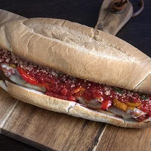 Fresh submarine sandwich on a wooden cutting board, filled with meat, vegetables, and sauce.