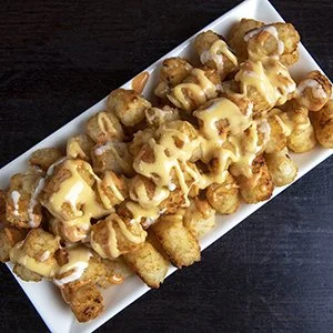 Tater tots topped with melted cheese sauce on a white rectangular plate.