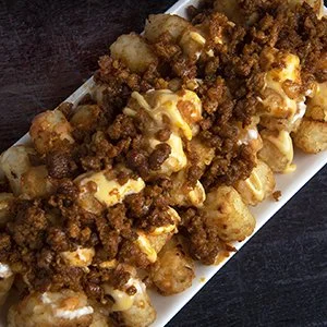 Close-up of loaded loaded tater tots topped with ground beef, cheese, and diced onions.