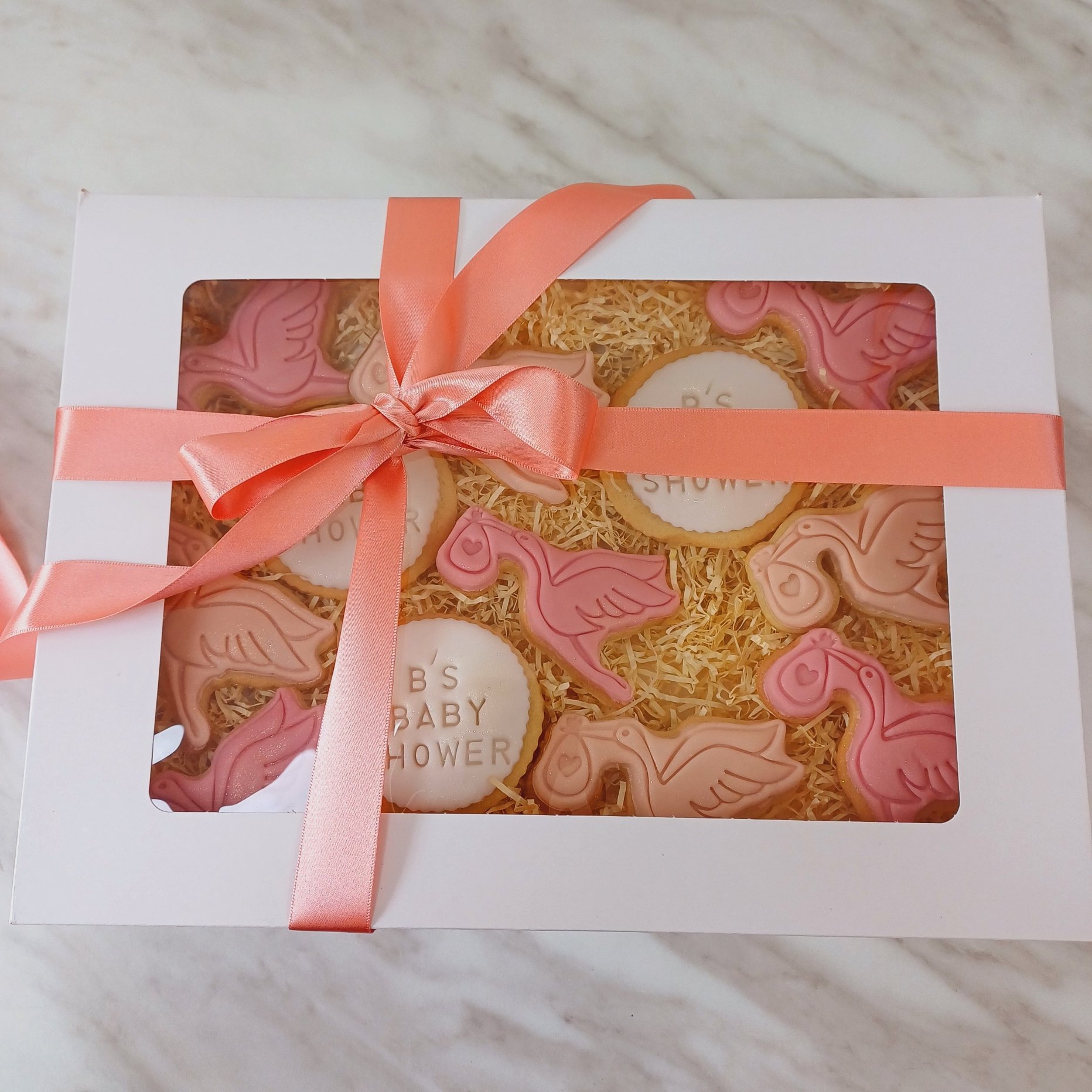 A delightful set of baby shower sugar cookies in soft pink and nude tones, beautifully crafted for a special occasion. The fondant-topped cookies are embossed with intricate designs, featuring a charming stork carrying a baby and round cookies person