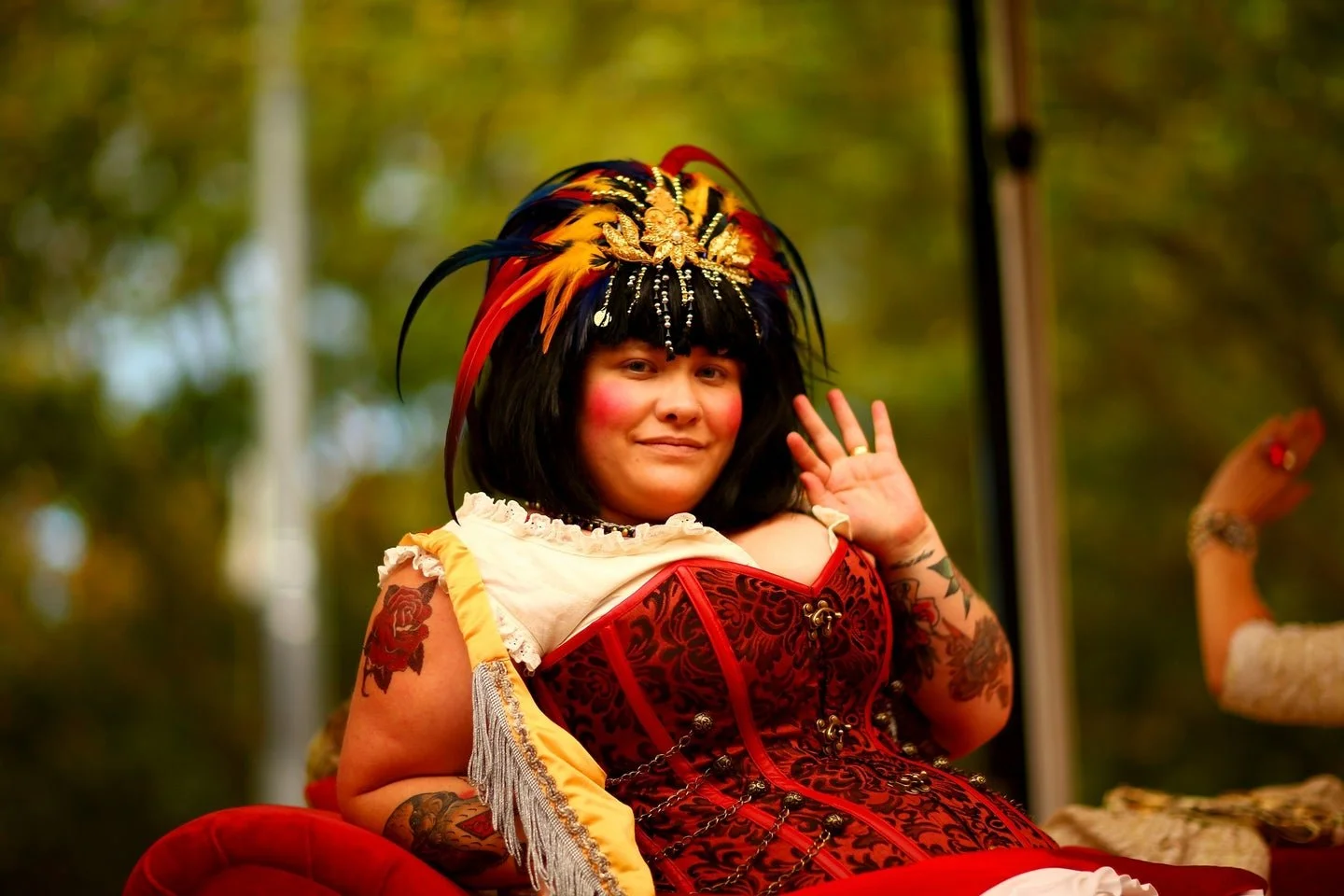 a beautiful human with black hair wearing a red corset and feathers in their hair