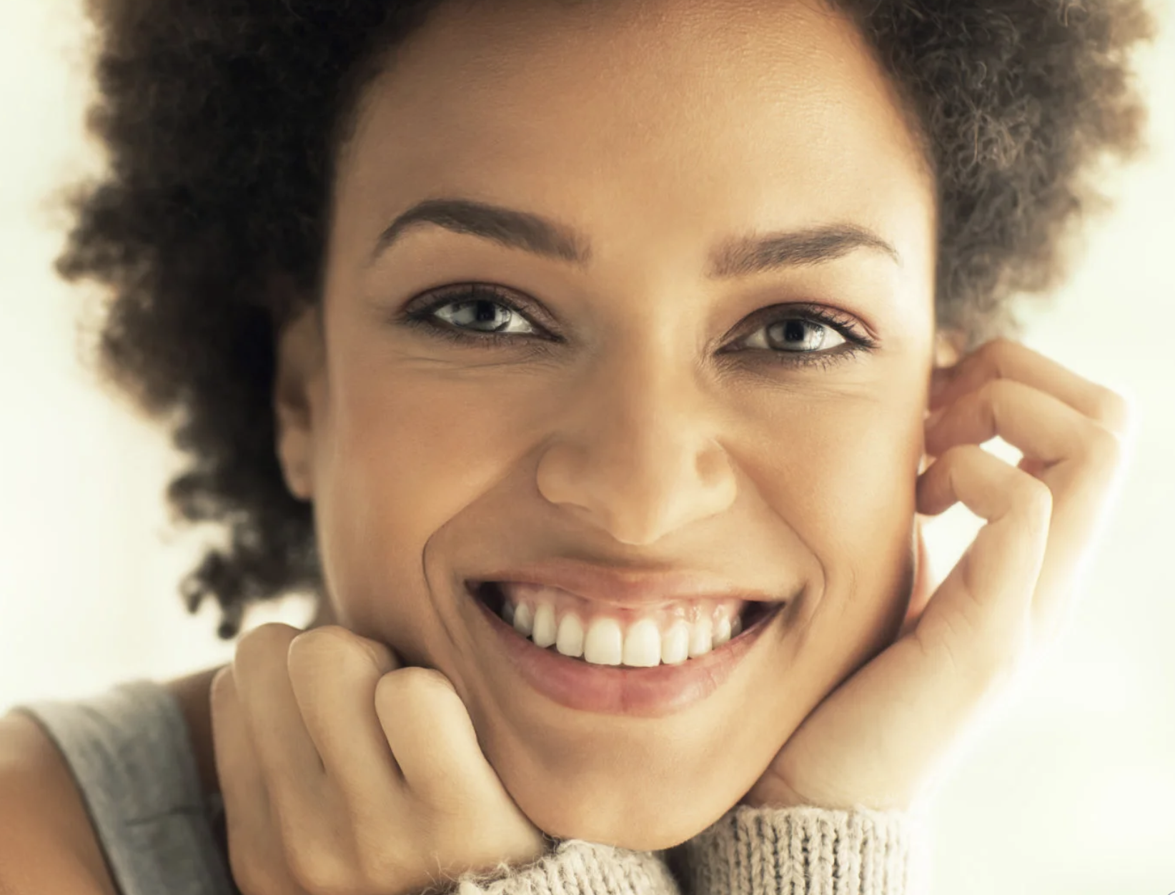 A smiling human with light brown skin and coily brown hair