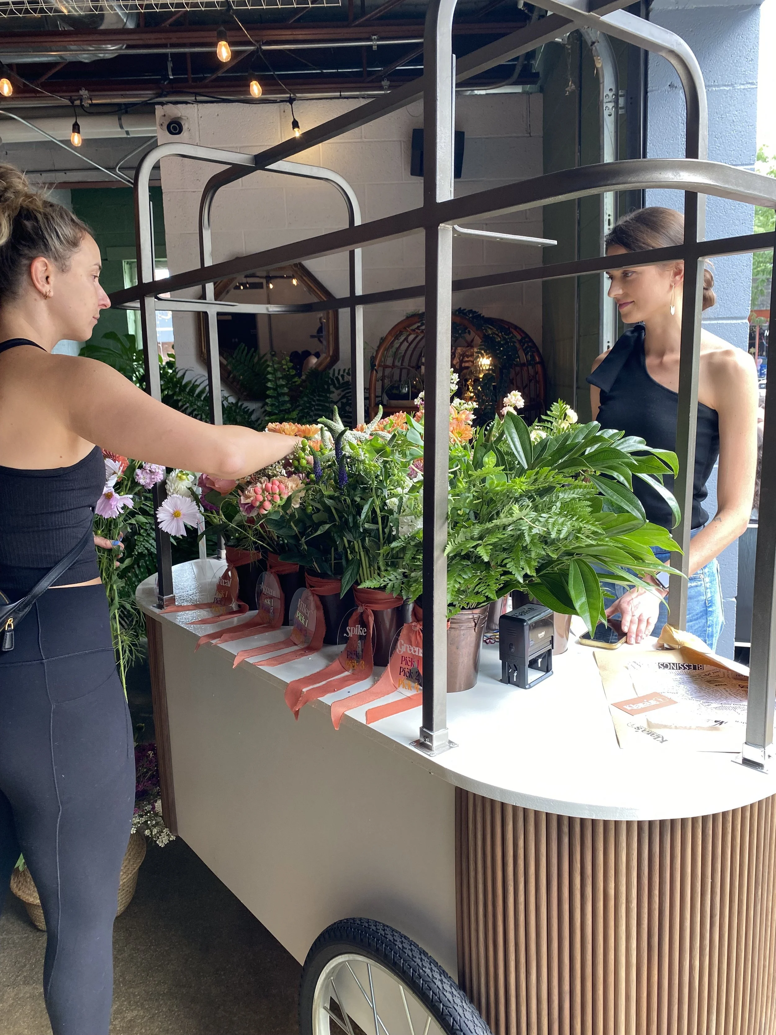 Metro Detroit Flower Cart, Klara's Bloom Haus selling various fresh flowers to a woman customer inside a store or market in Royal Oak, MI.