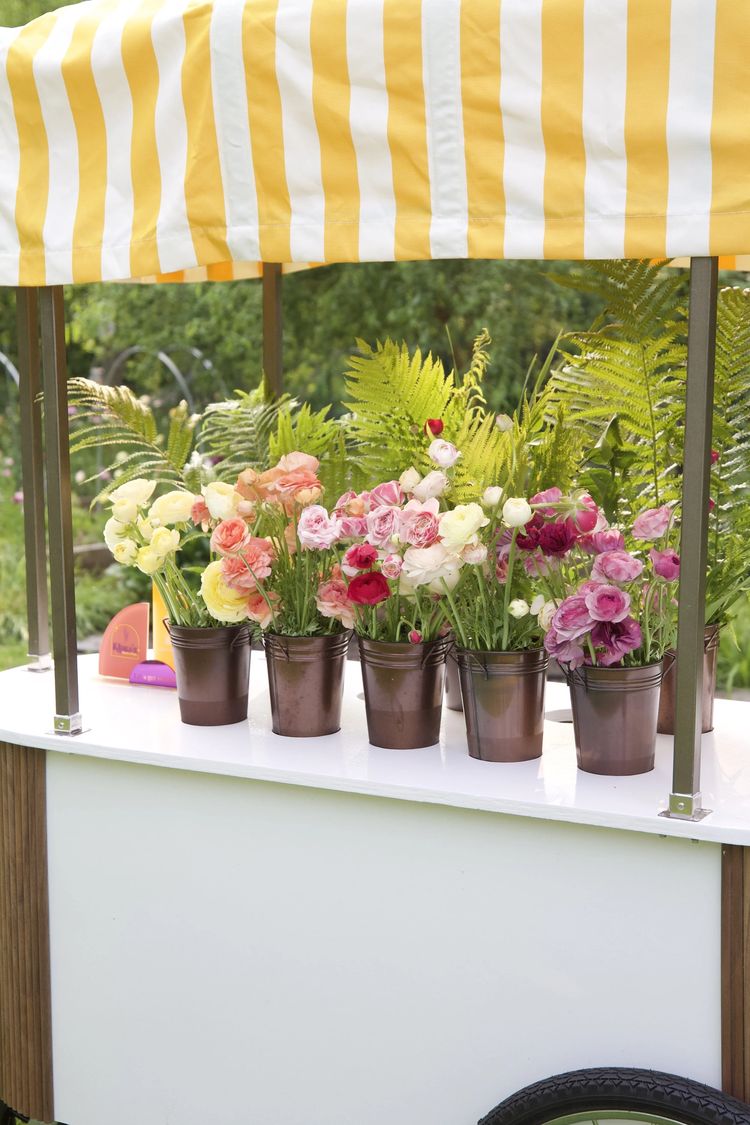 Colorful flower cart with pink, white, and red blooms under a yellow and white striped canopy at a bridal shower private event.