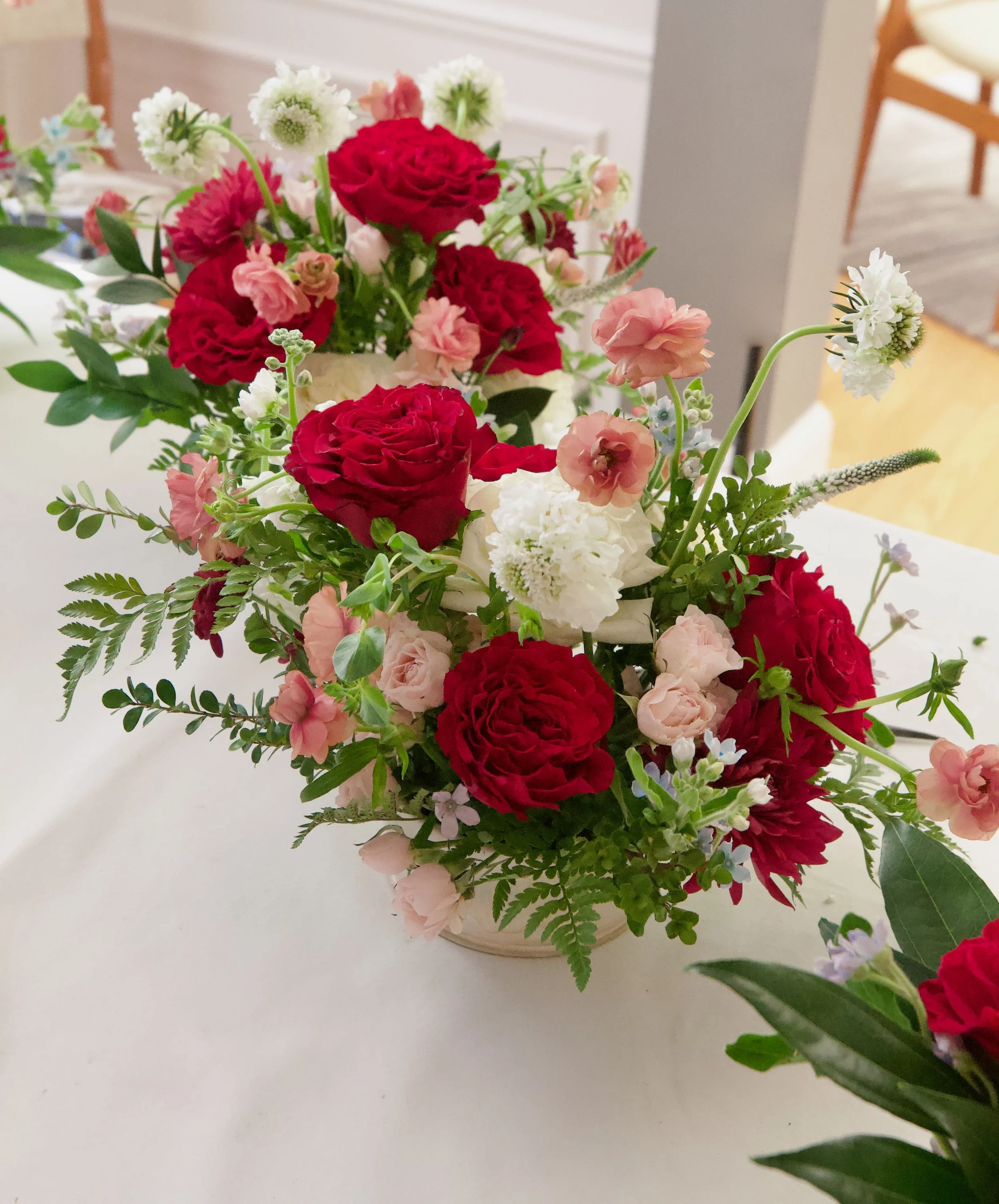 A floral arrangement with red, pink, white, and green flowers in a vase on a white surface.