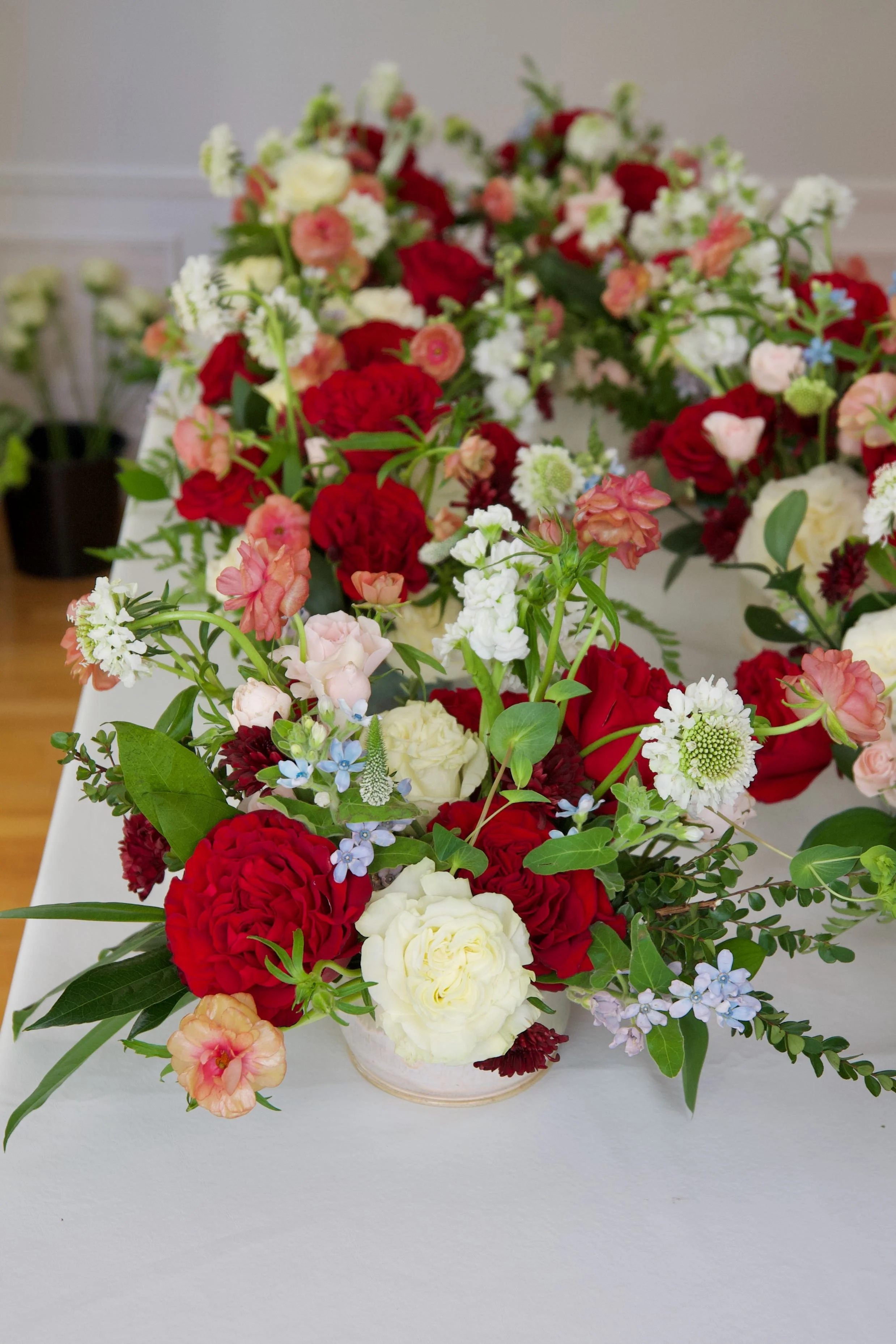 A colorful flower arrangement featuring red, white, pink, and blue flowers with green leaves on a white table.