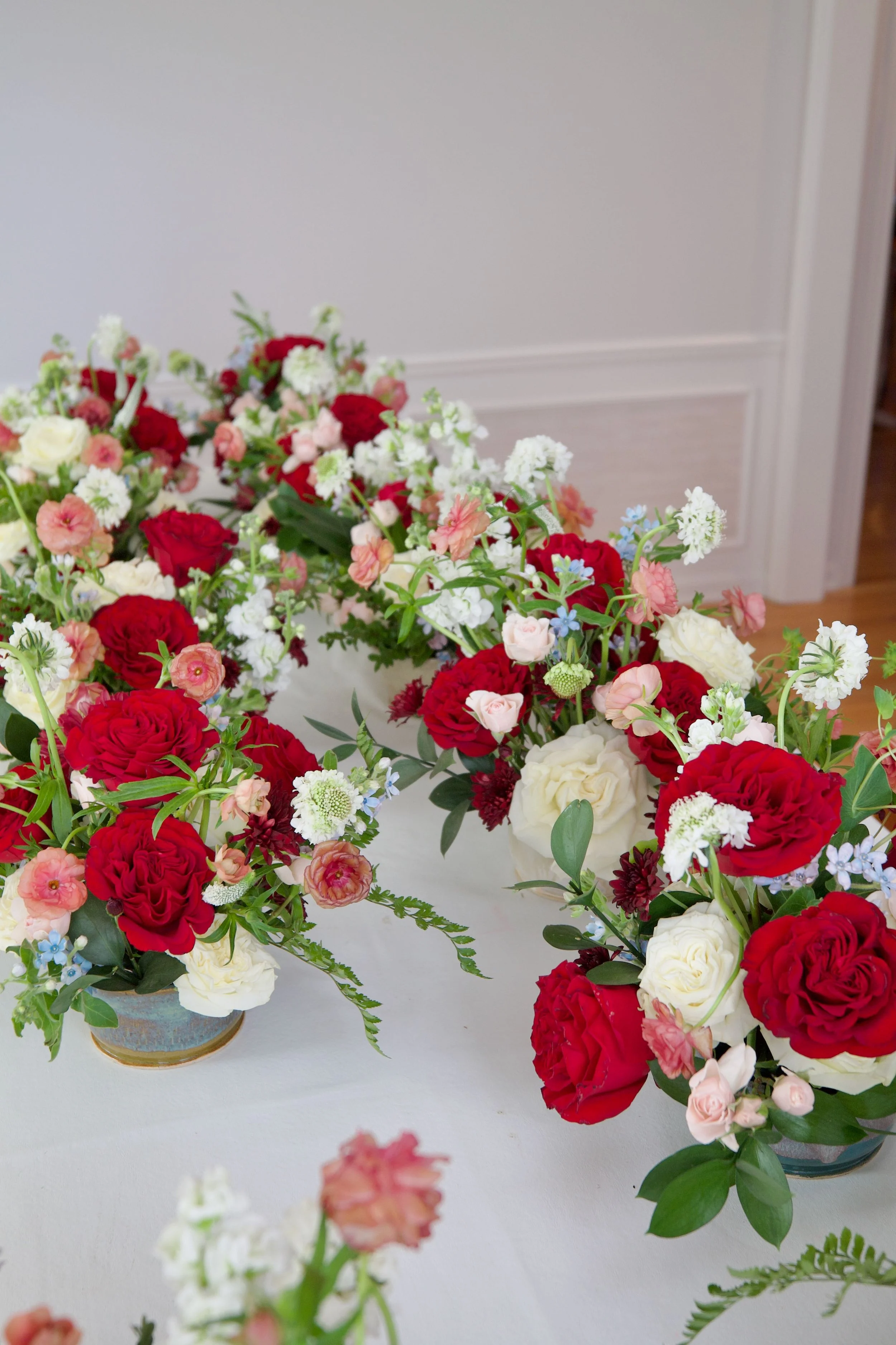 Vases with red, white, pink, and light blue flowers arranged on a white table, with a plain wall in the background.