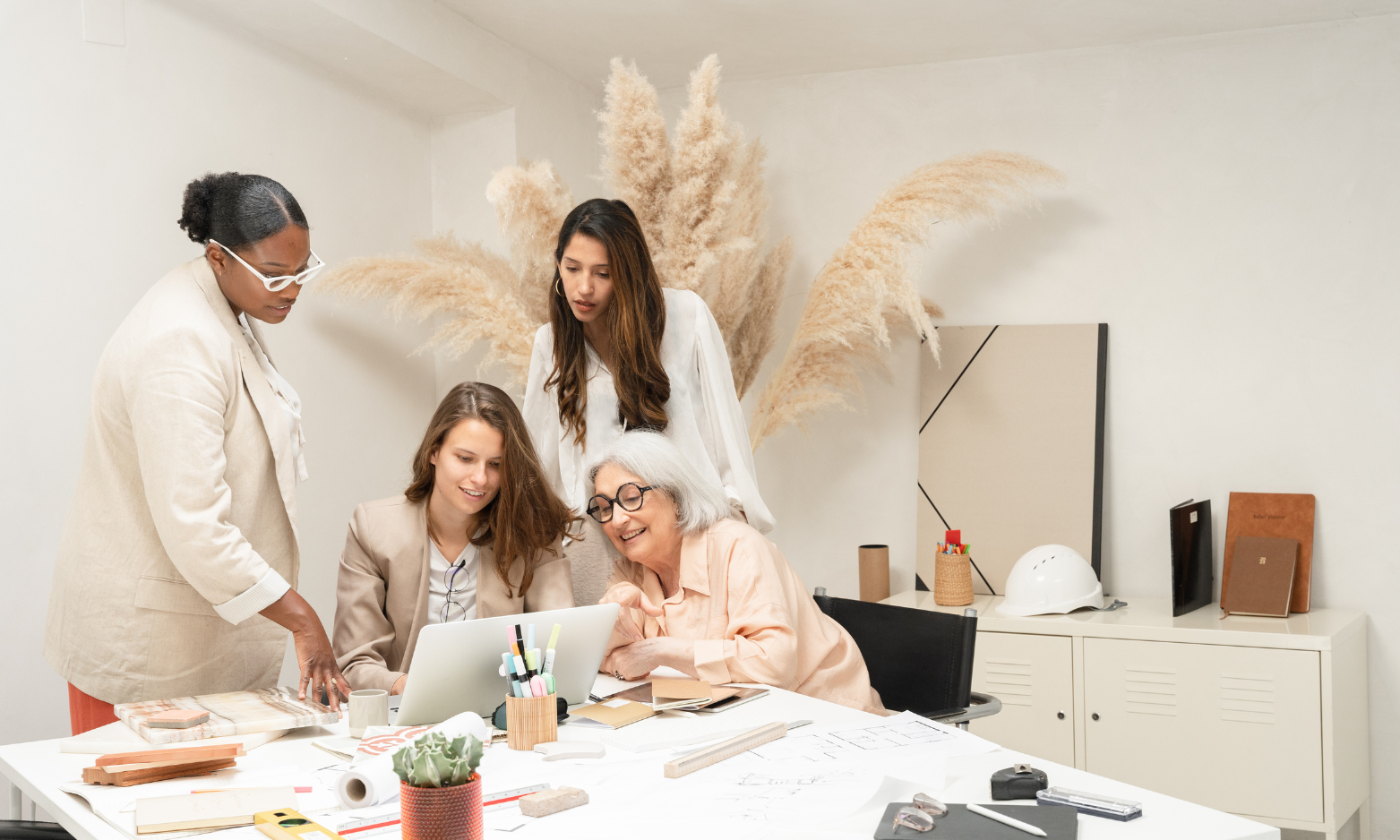 four women in neutral clothing looking at one laptop happily