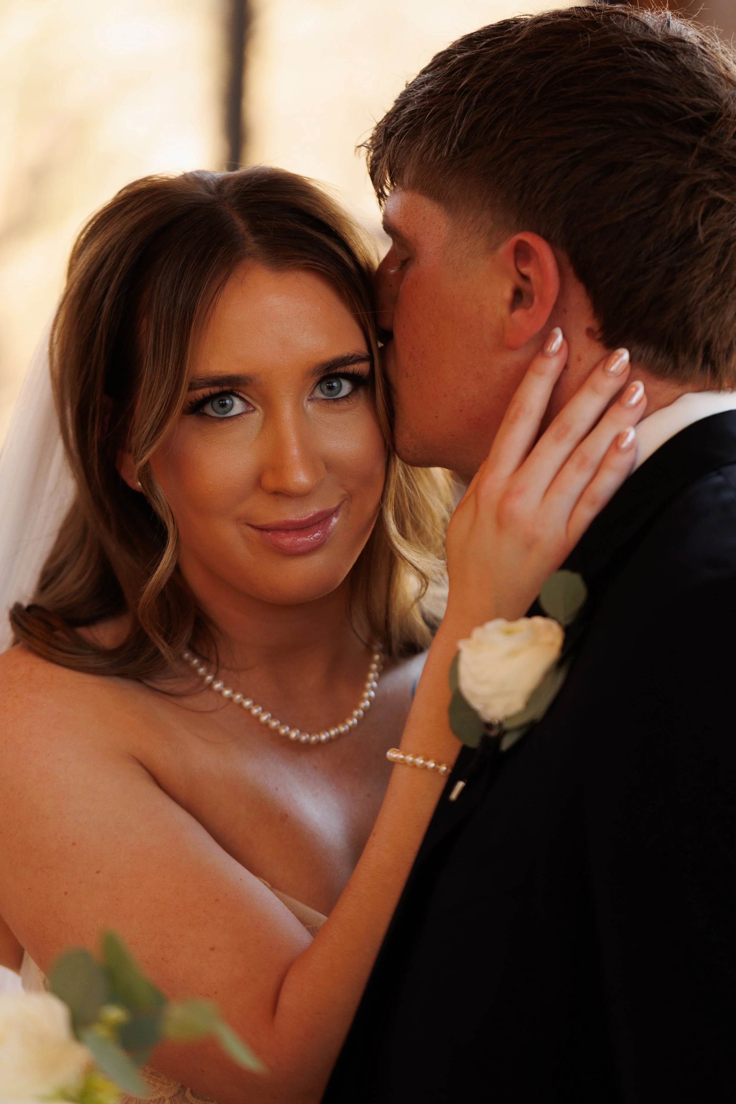 A bride and groom sharing a tender moment on their wedding day at Thunderbird Chapel, with the groom kissing the bride's temple as she looks at the camera. Taken by top-rated wedding photographers in Oklahoma City
