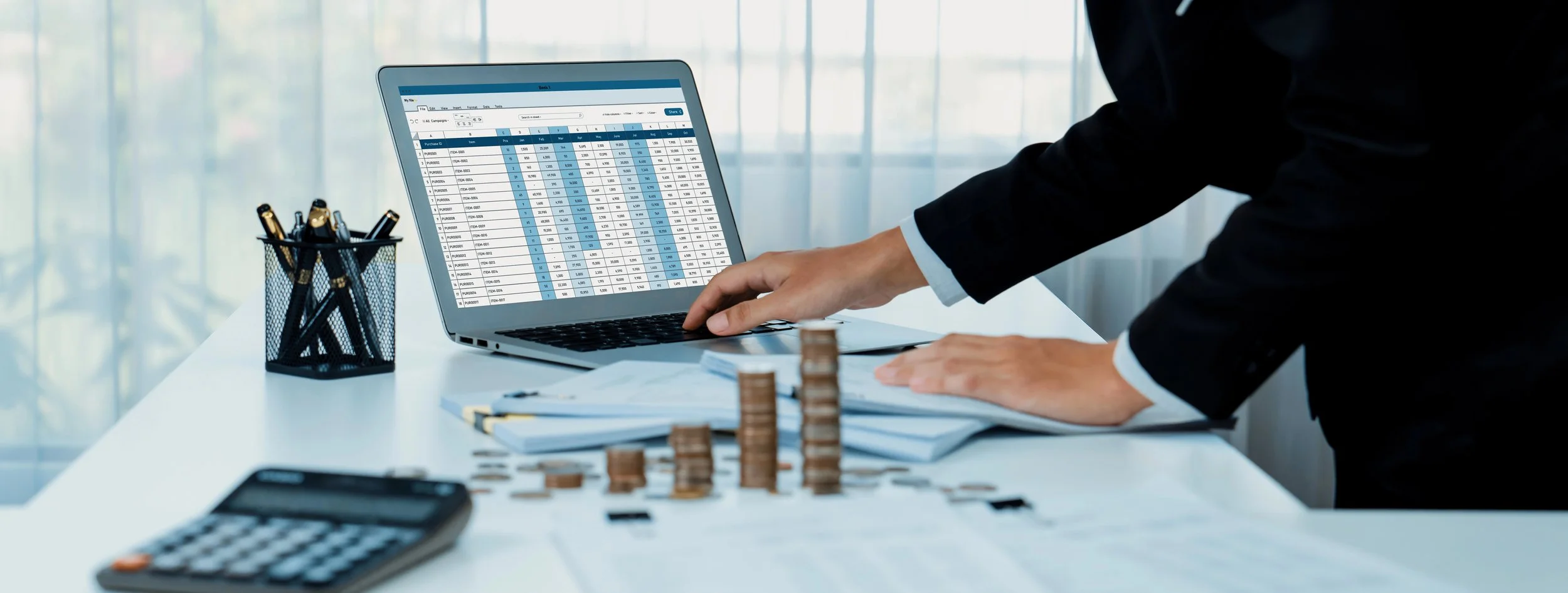 Analyst reviewing financial statements on a laptop with a calculator and coin stacks during a quality of earnings (QoE) review.