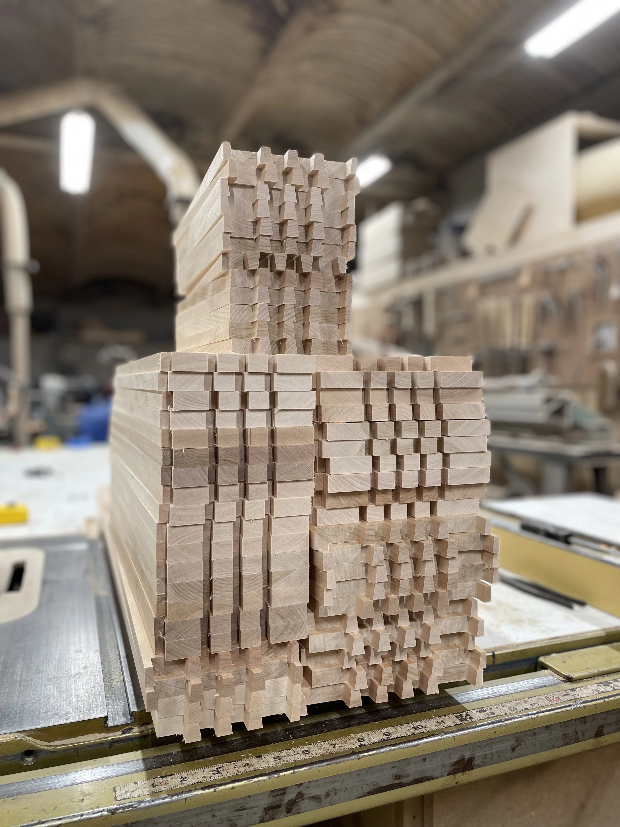 Stacked bundles of wooden pieces with various shapes and notches in a woodworking shop.