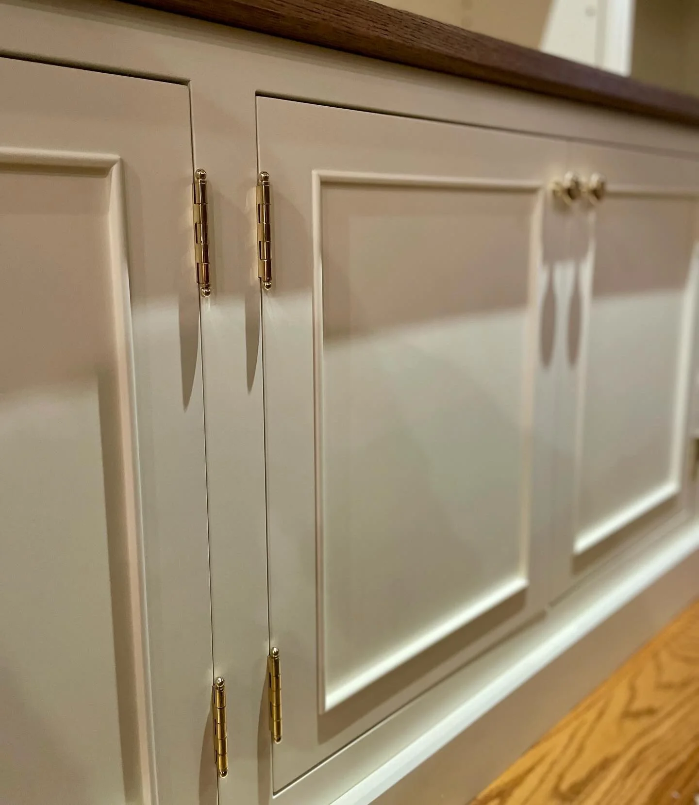 Close-up of white kitchen cabinets with gold hinges and knobs, and a wooden countertop.