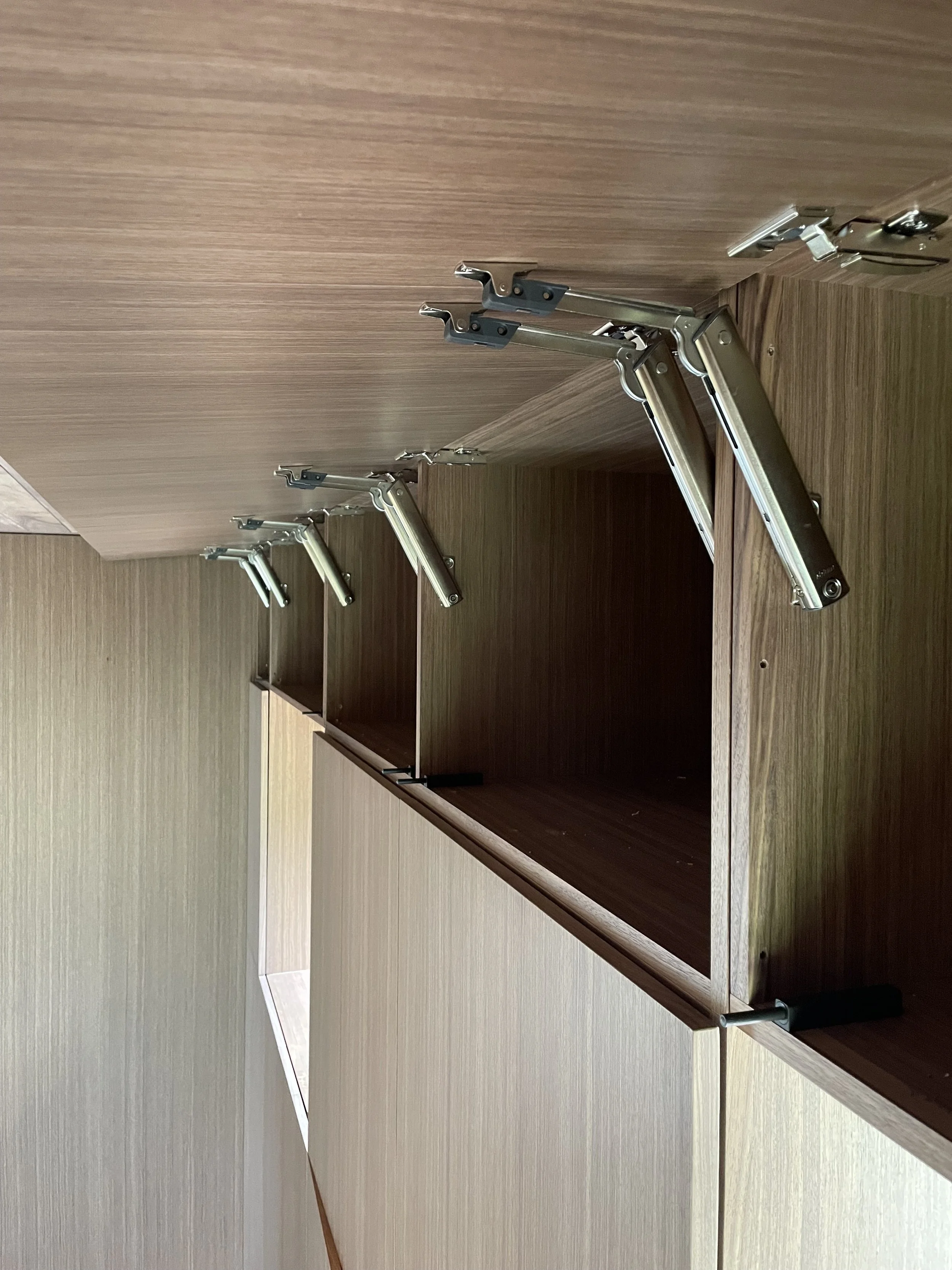 Wooden cabinet with metal hinge supports inside, some hinges are extended and open, and some are closed.