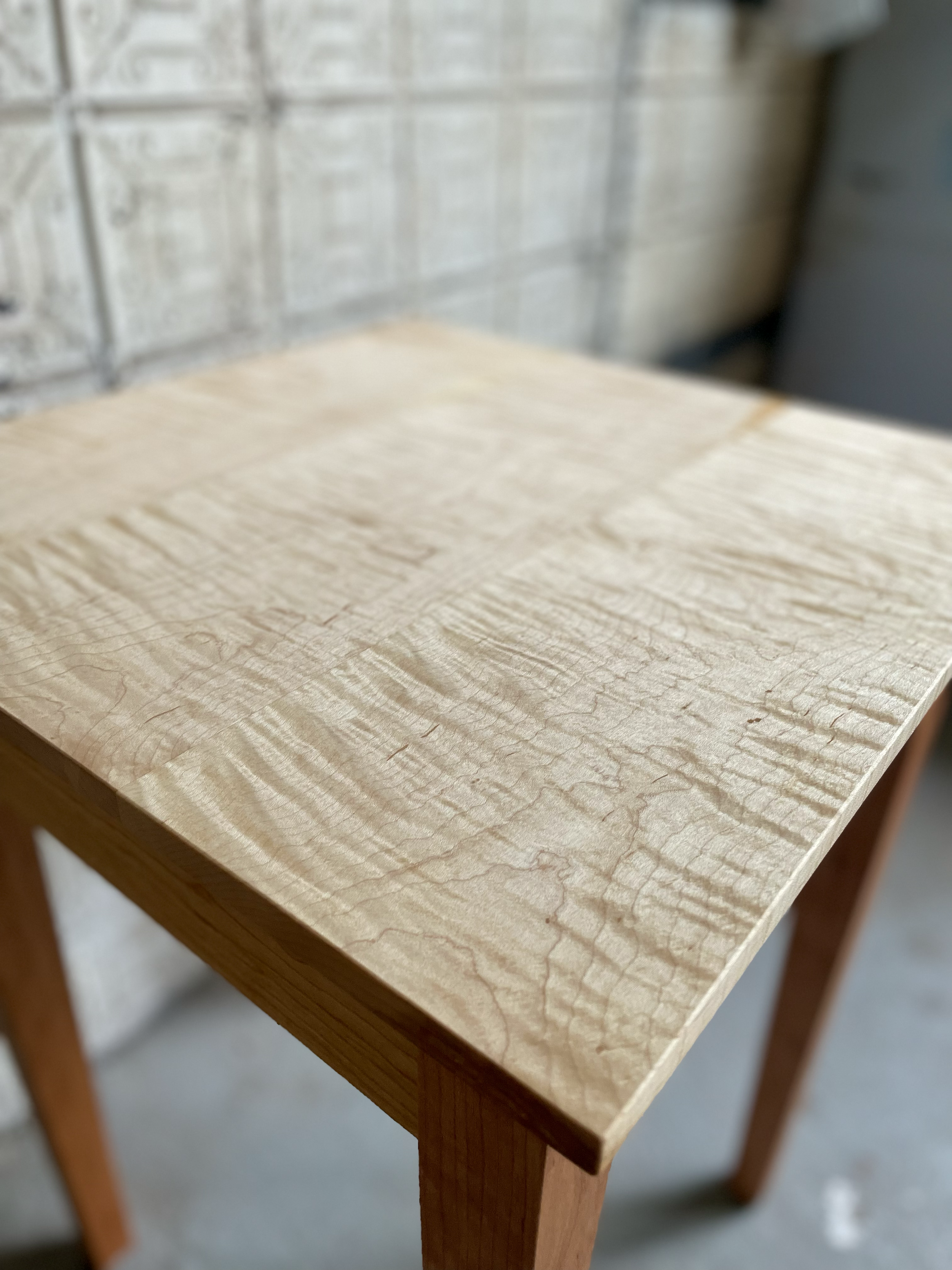 Close-up of a wooden table with a smooth, light-colored top and sturdy legs, in a workshop setting.